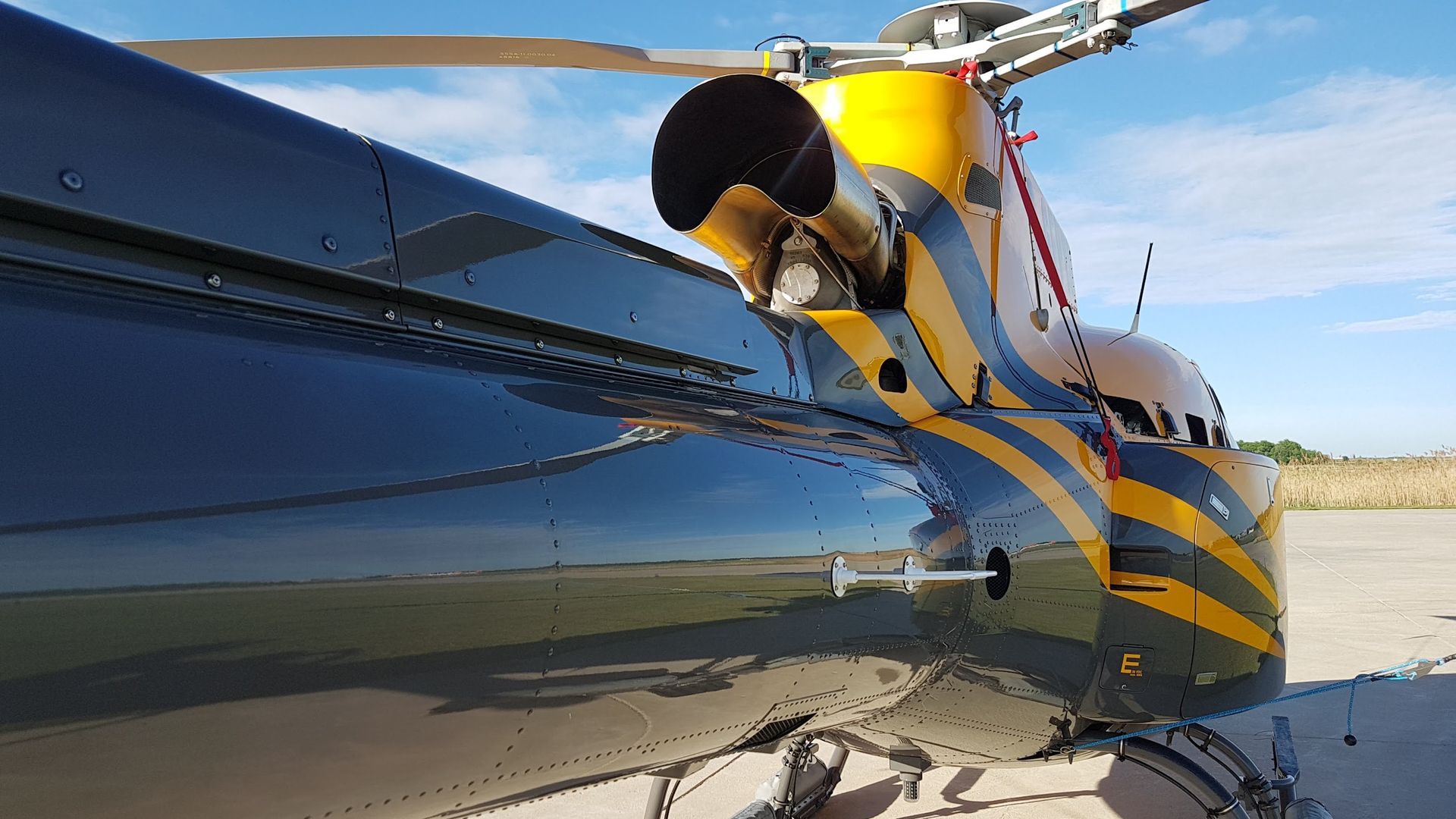 Rear section of a black and yellow helicopter parked outdoors on a sunny day.