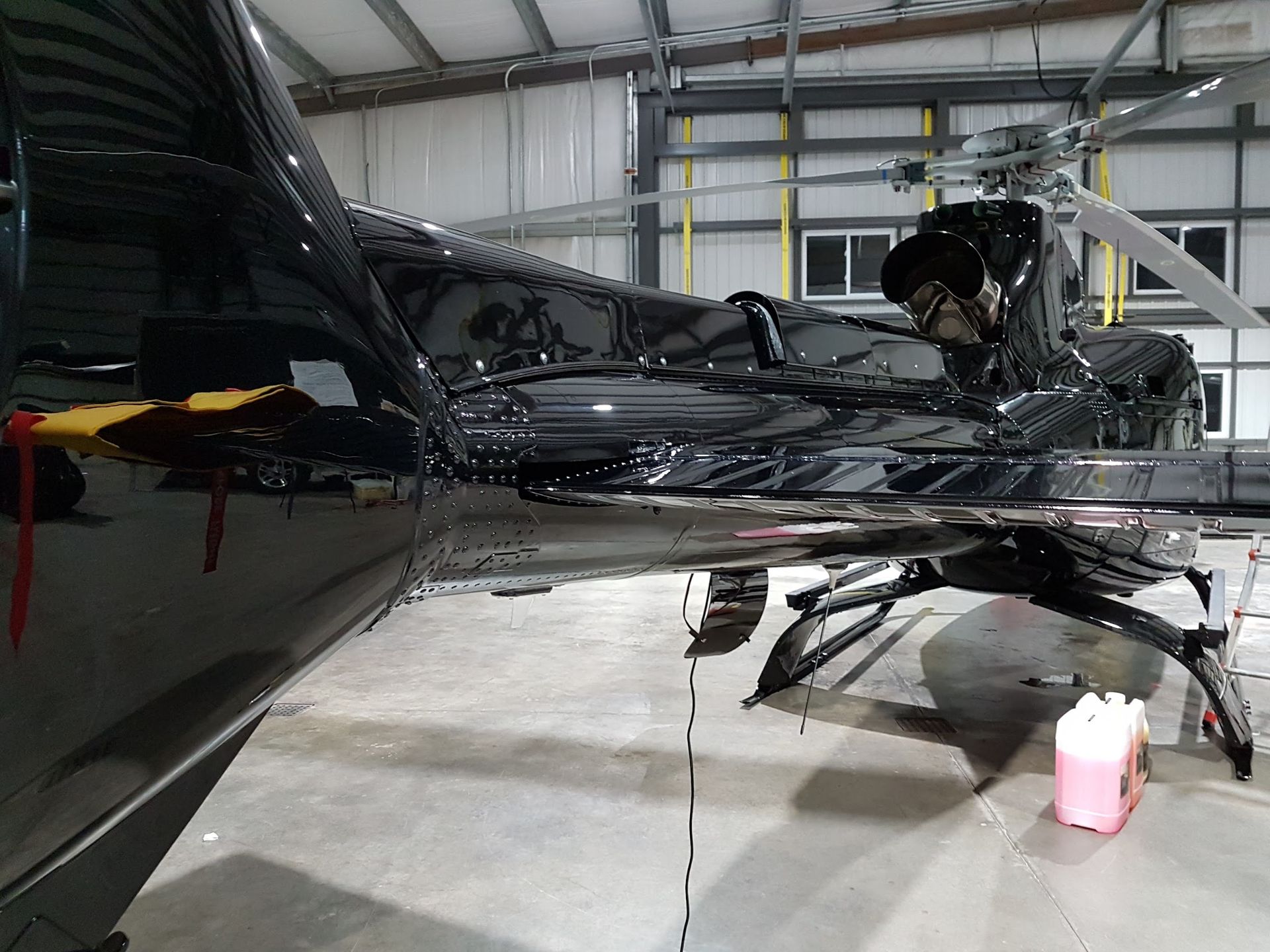 Black helicopter in a hangar; side view showing tail, rotor, and landing gear.
