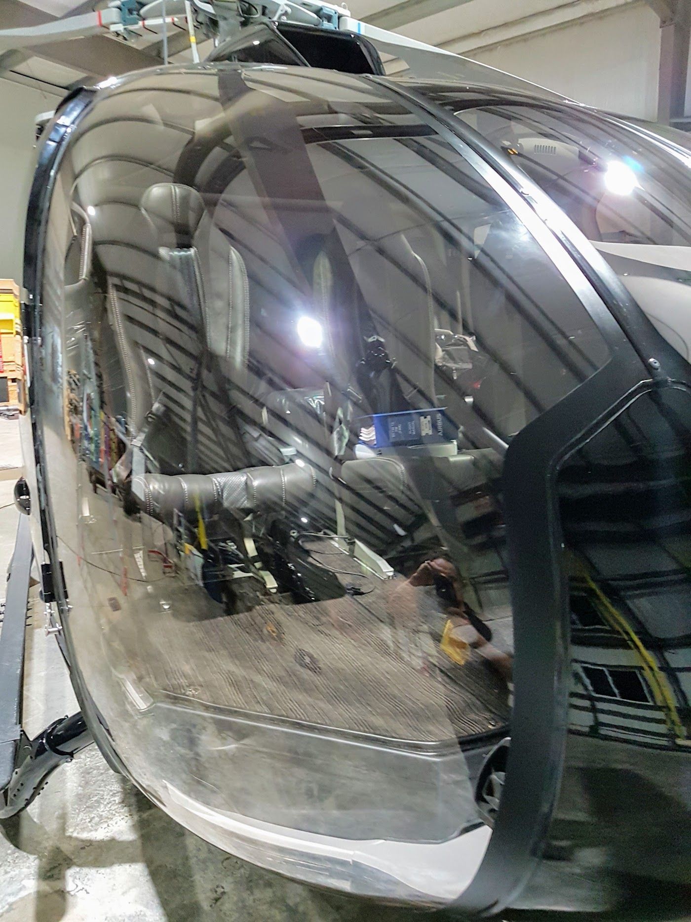 Close-up of helicopter cockpit reflecting a hangar interior with lights and equipment.