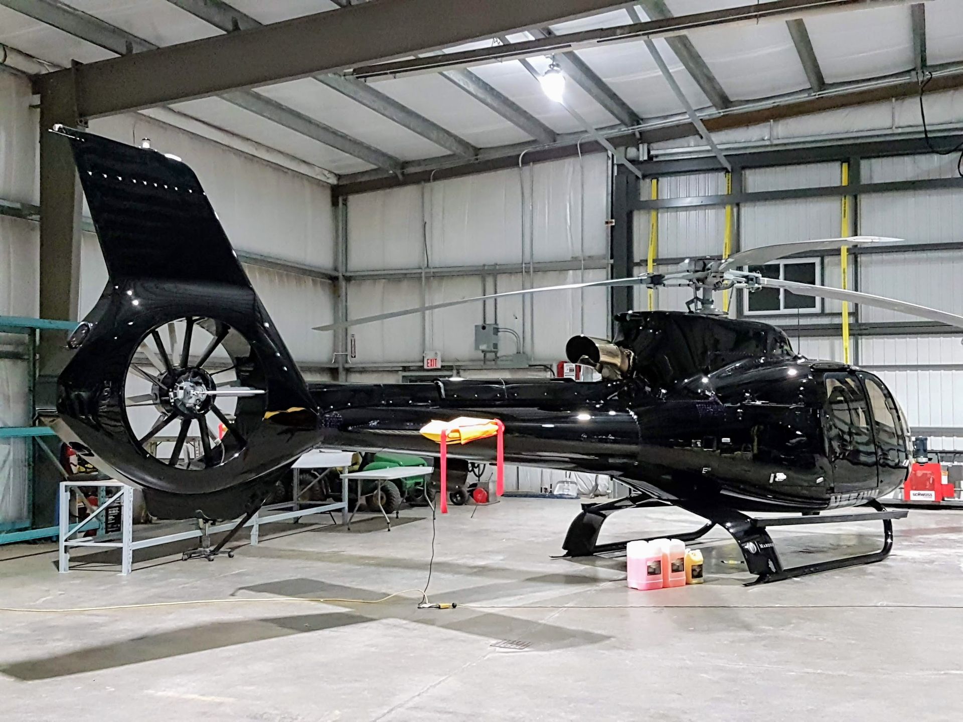 Black helicopter inside a hangar with the tail rotor visible, set against the walls and ceiling.