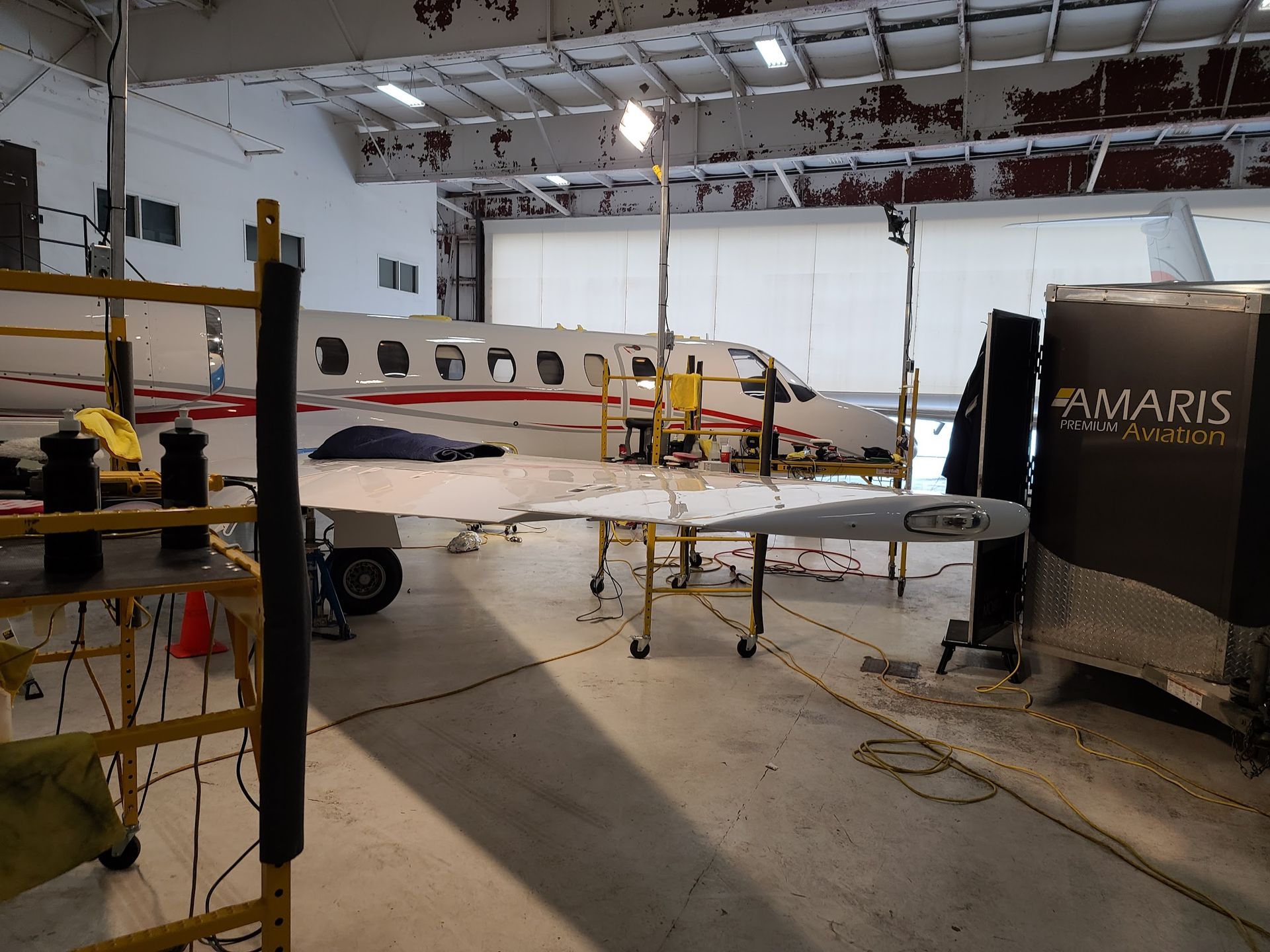 Airplane wing being worked on in a hangar, with scaffolding and AMARIS branding visible.