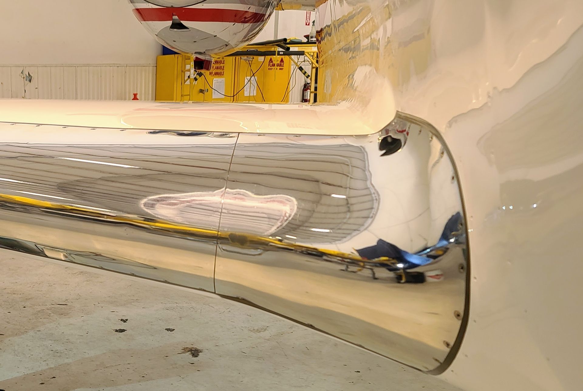 Shiny, curved chrome object reflecting a hangar interior with equipment and a floor.