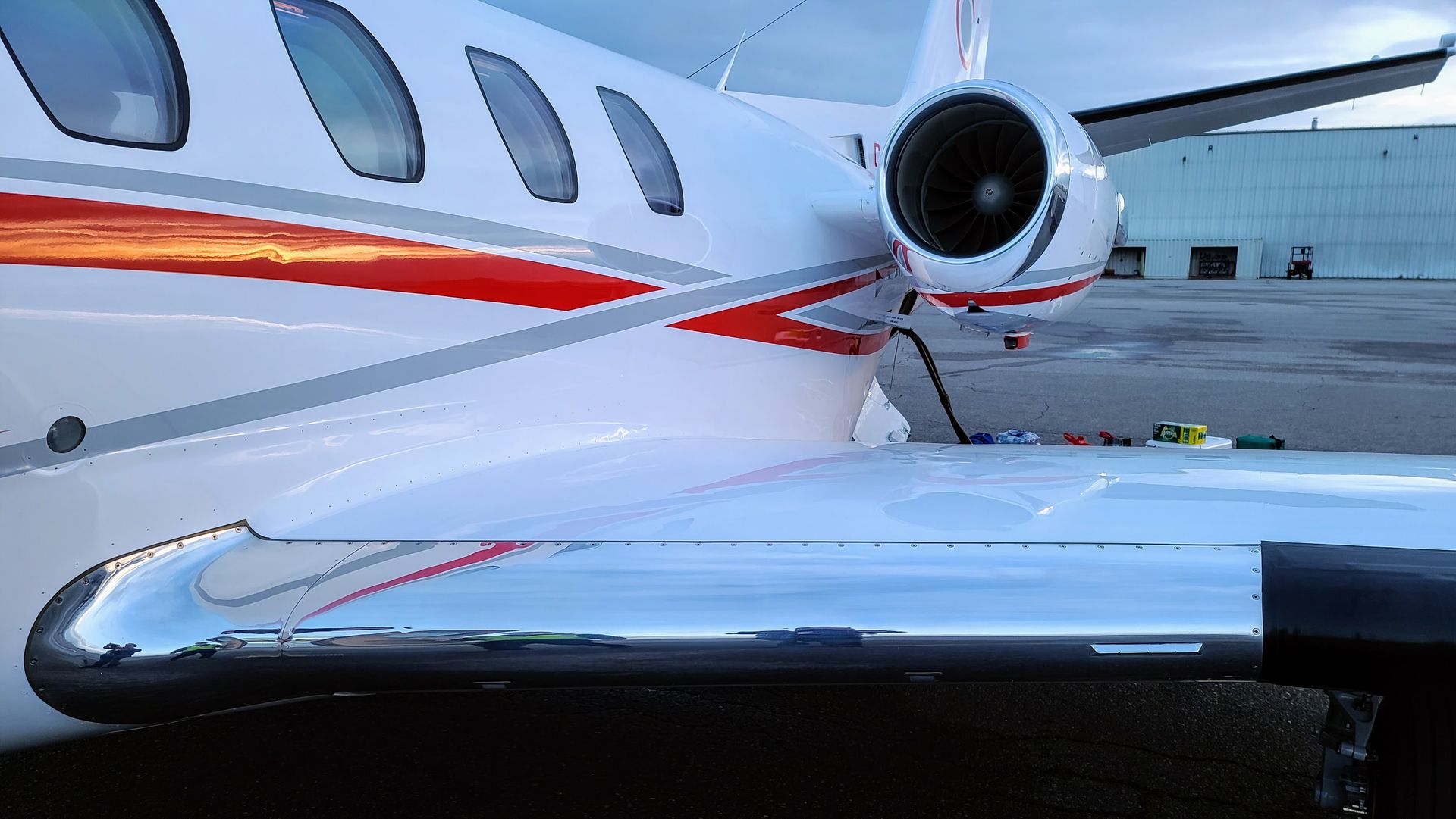White and red jet airplane wing, parked near a building.