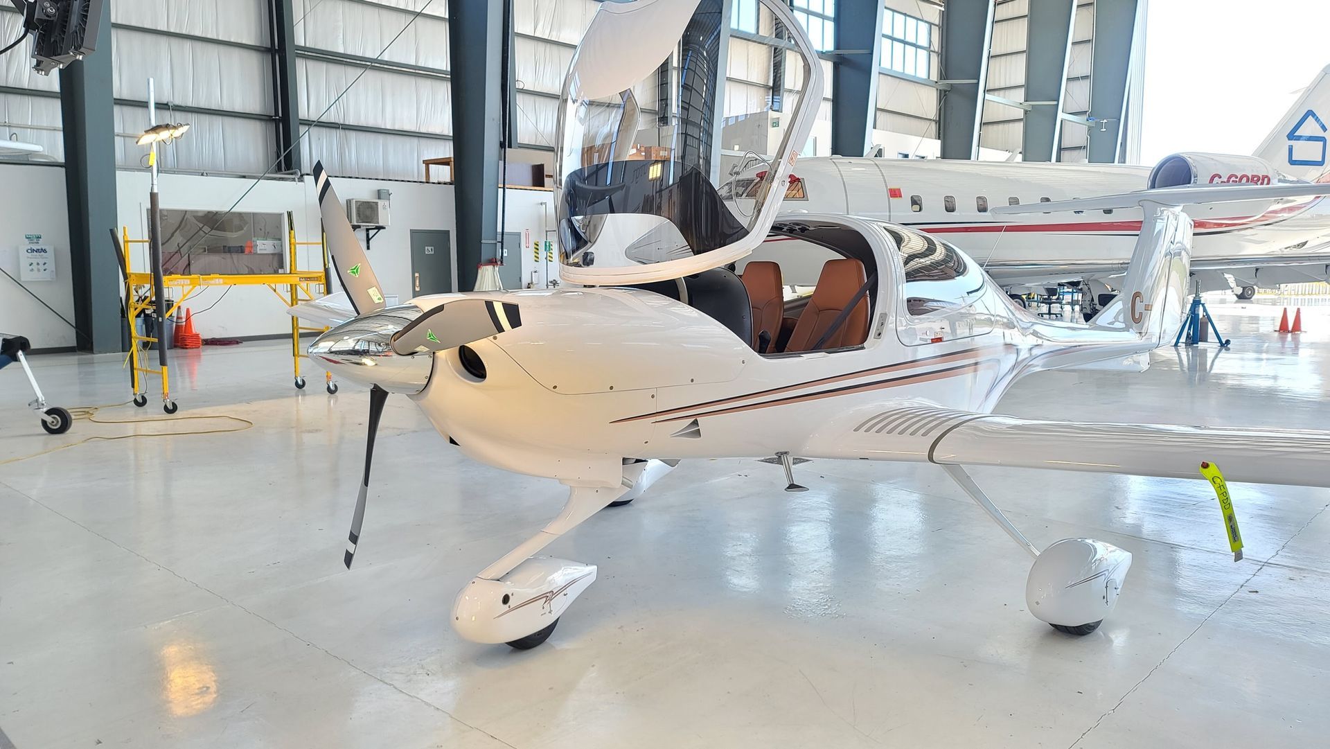 White airplane with open doors in a hangar, another plane in background.