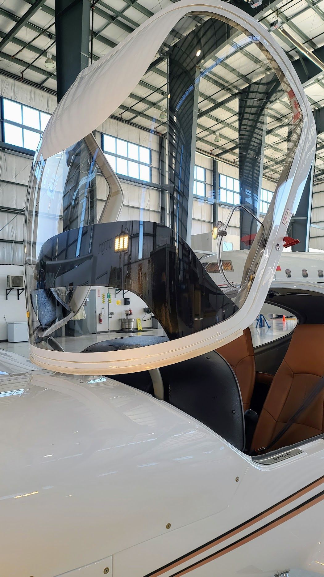 Cockpit of a white aircraft with an open, transparent canopy in a hangar.