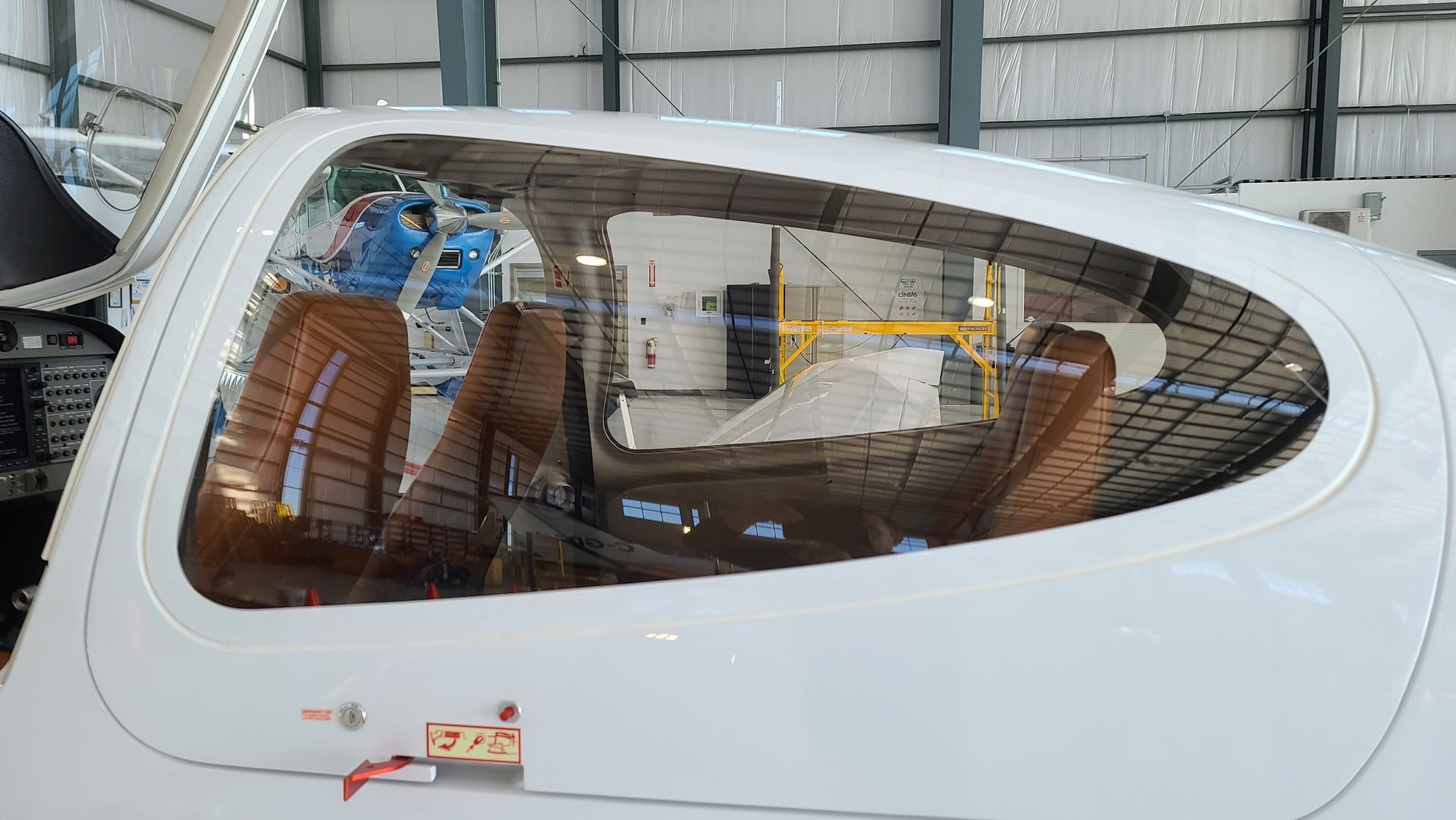 Side view of a white airplane cockpit with clear windows, showing brown leather seats inside a hangar.