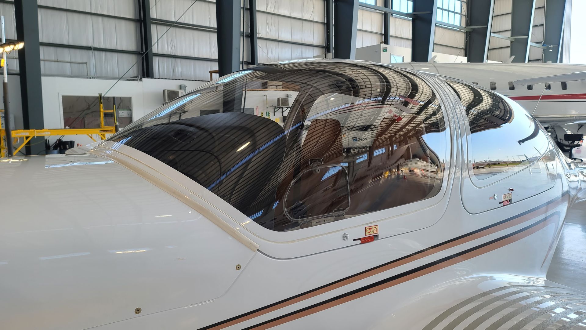 White airplane cockpit with a clear bubble canopy in a hangar.