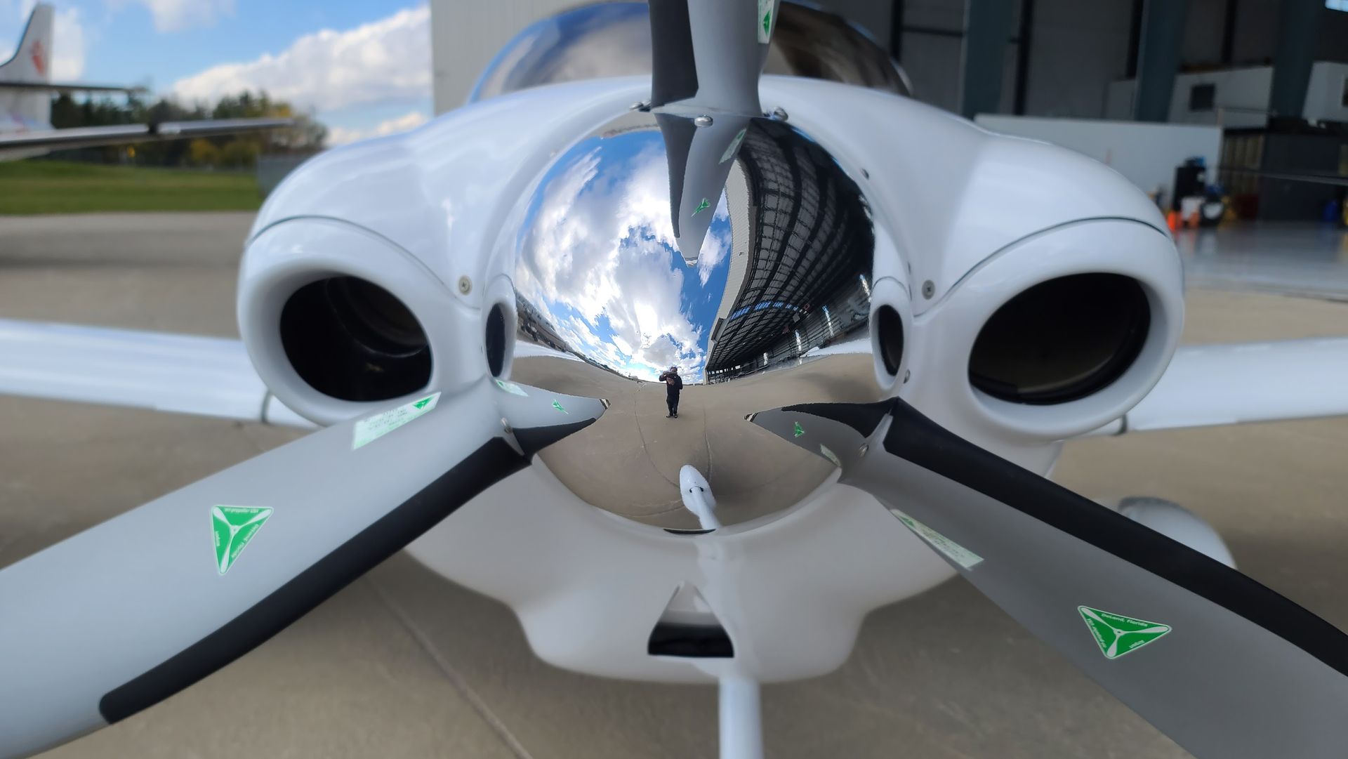 White airplane with two propellers, reflected hangar in the polished nose, on a runway.