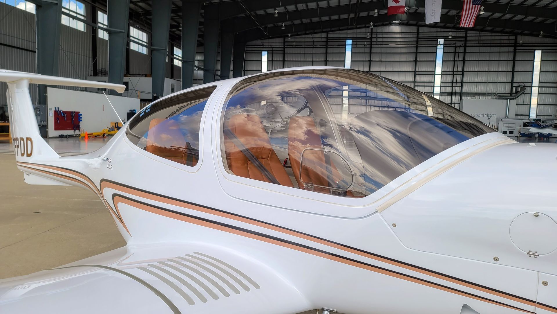 White and bronze airplane parked inside a hangar; clear canopy reveals brown leather interior.