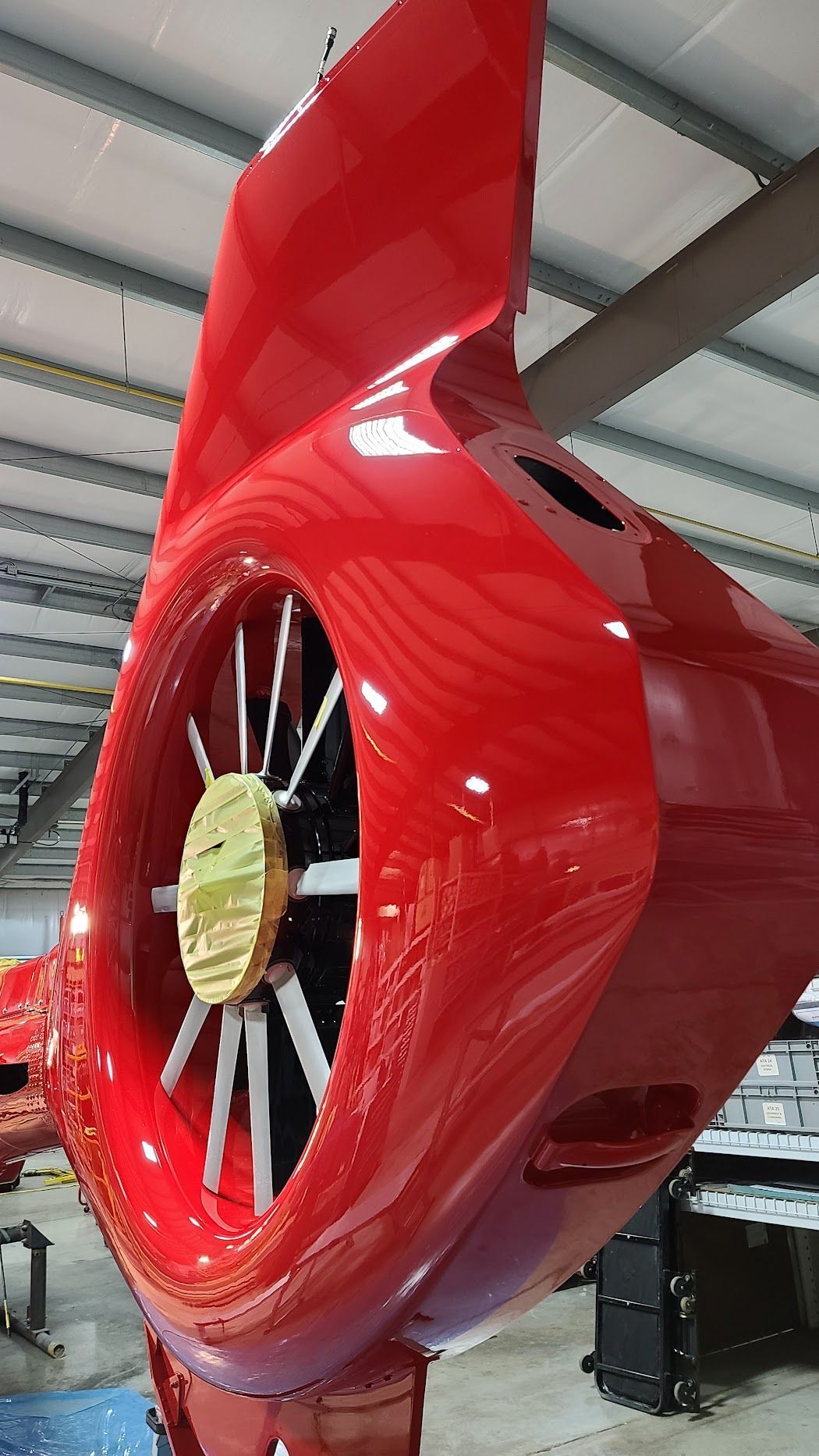 Red aircraft tail with fan blades, hanging in a workshop, bright and glossy.