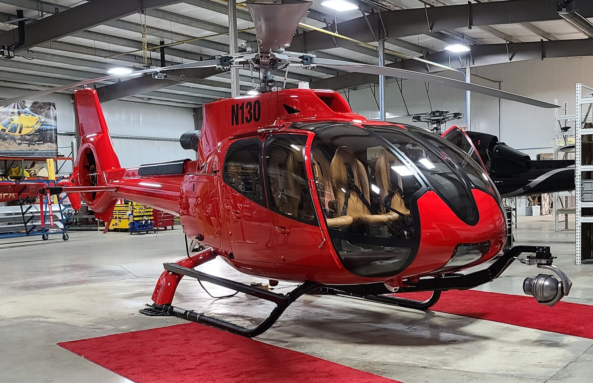 Red helicopter inside a hangar with a red carpet. The helicopter has visible cabin seating.