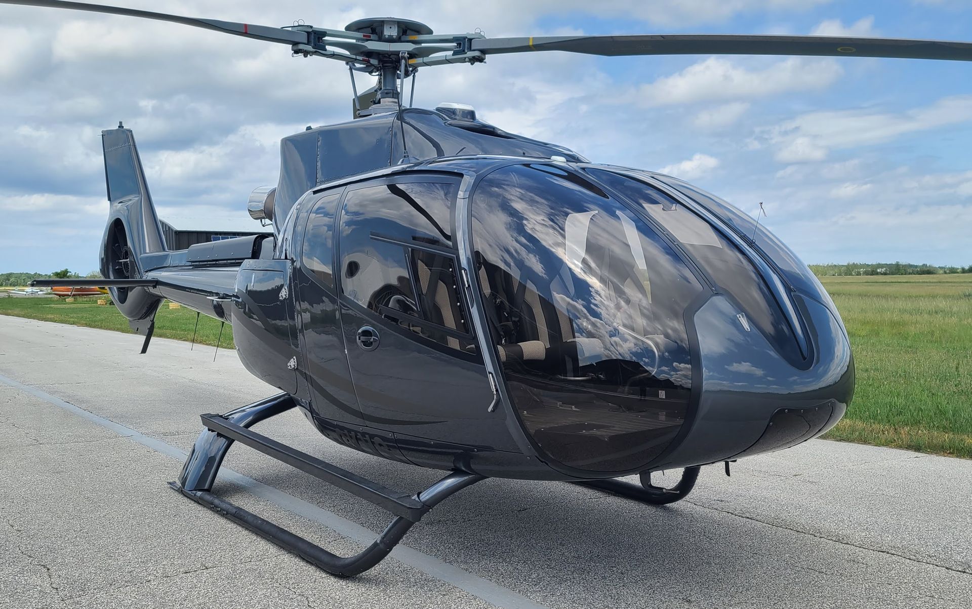 Black helicopter on a concrete landing strip with a cloudy sky in the background.