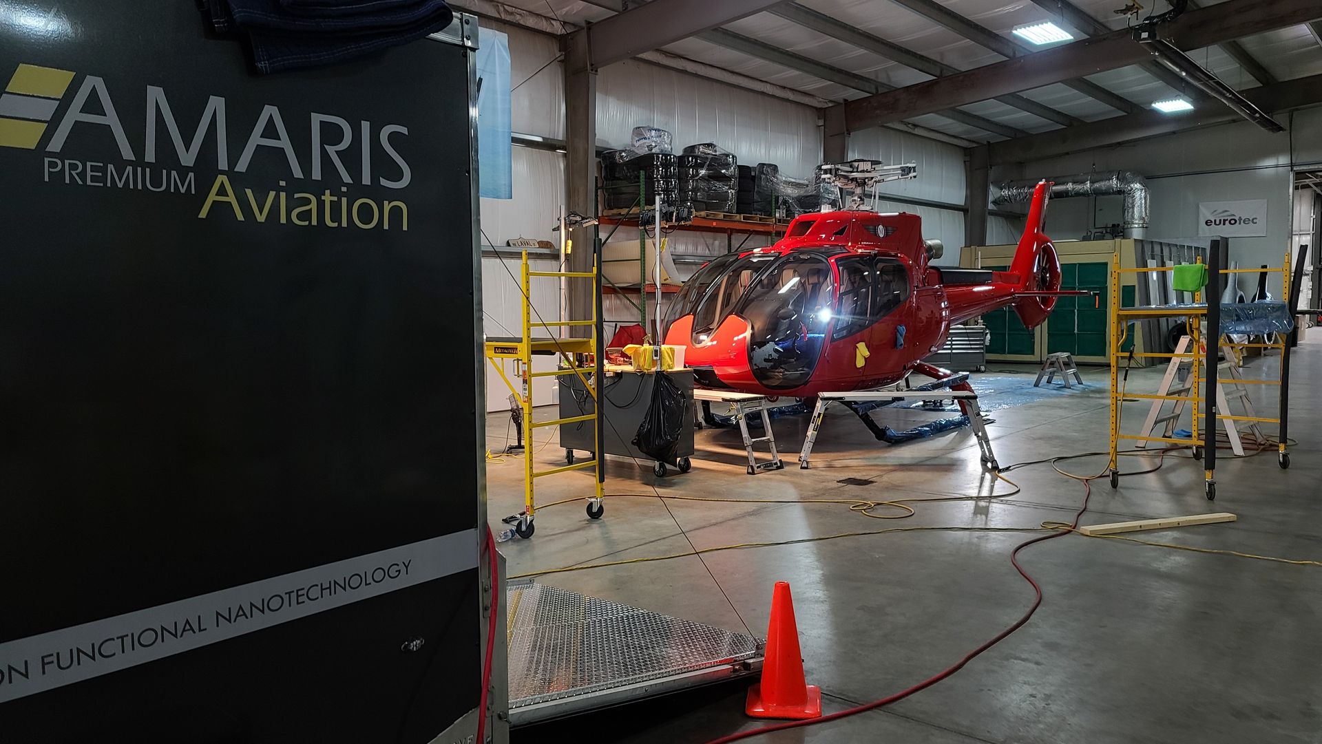 Red helicopter in a hangar with the Amaris Premium Aviation logo on a black cart.