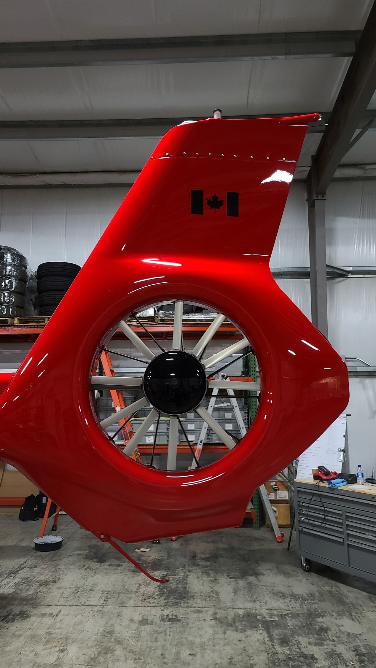 Red helicopter tail with Canadian flag. In a warehouse. Tail rotor visible.
