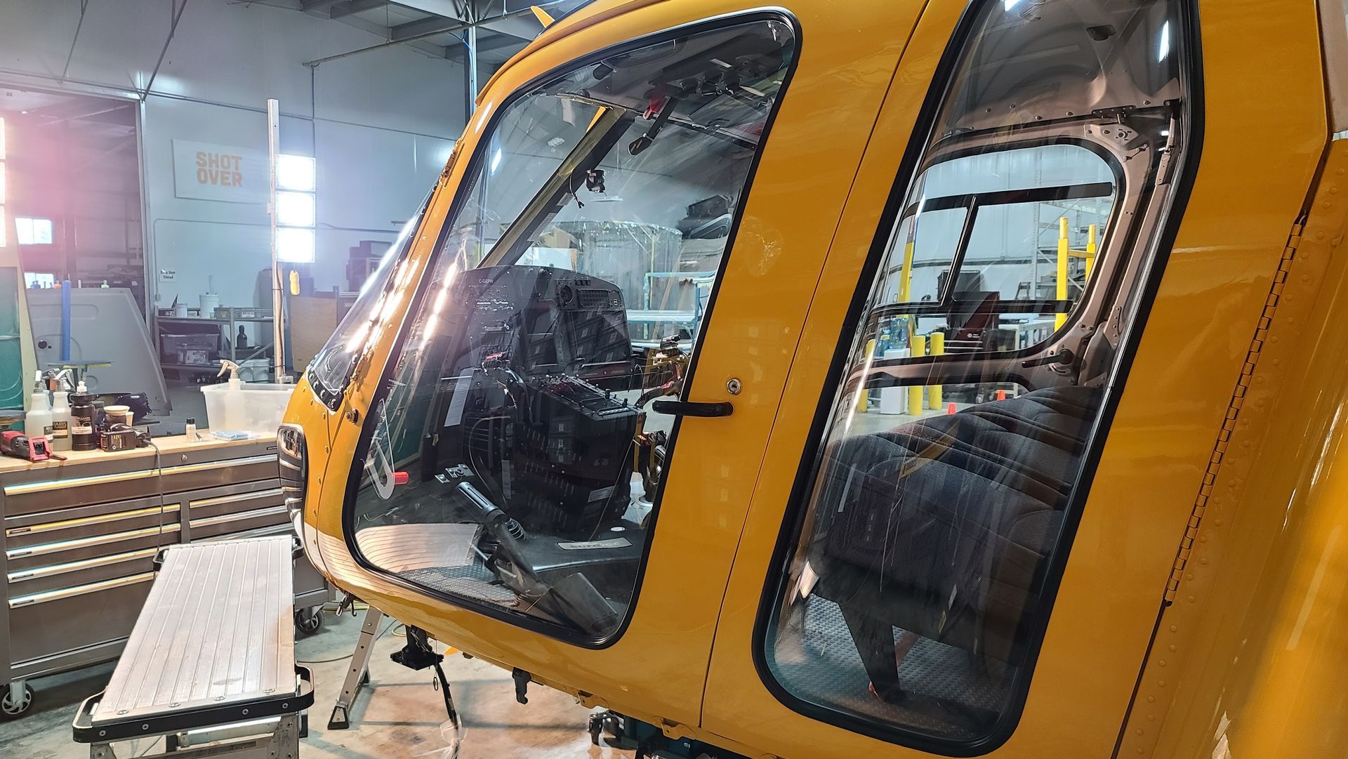 Yellow helicopter cockpit interior in a workshop, window open.