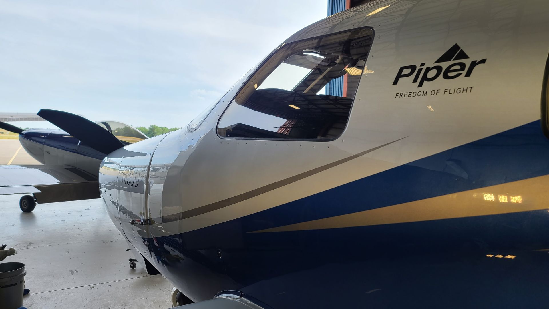 Silver and blue Piper M500 turboprop aircraft parked in a hangar.