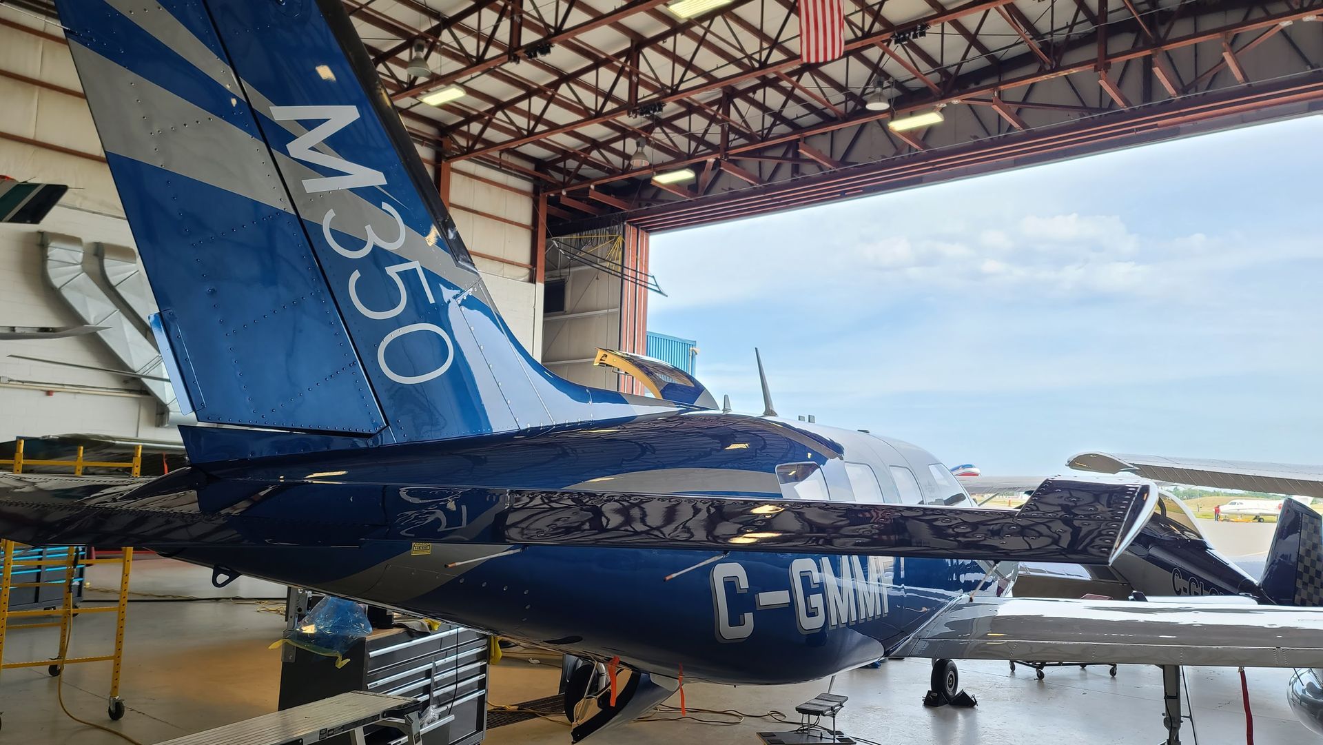 Blue and silver M350 airplane tail in a hangar, with the registration C-GMMH visible.
