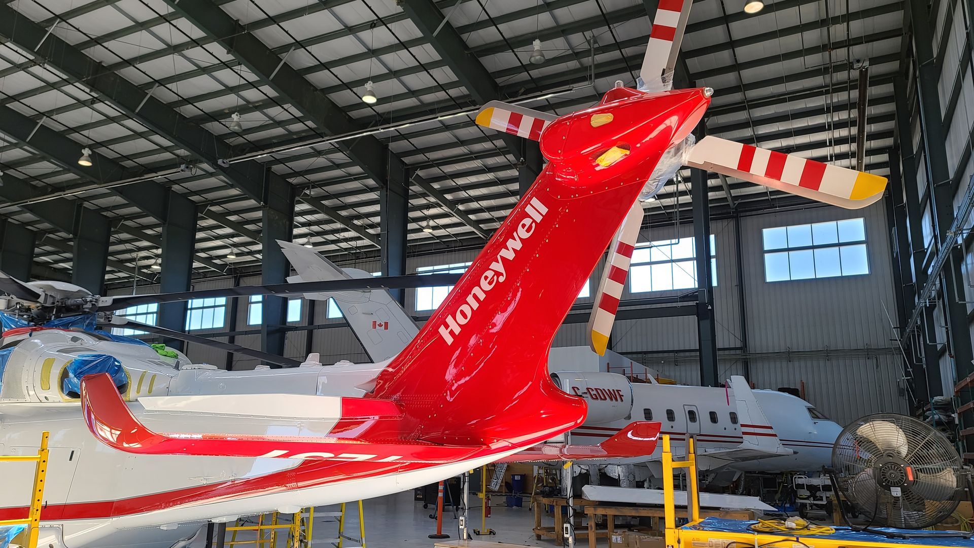 Red and white Honeywell helicopter in a hangar with other aircraft.