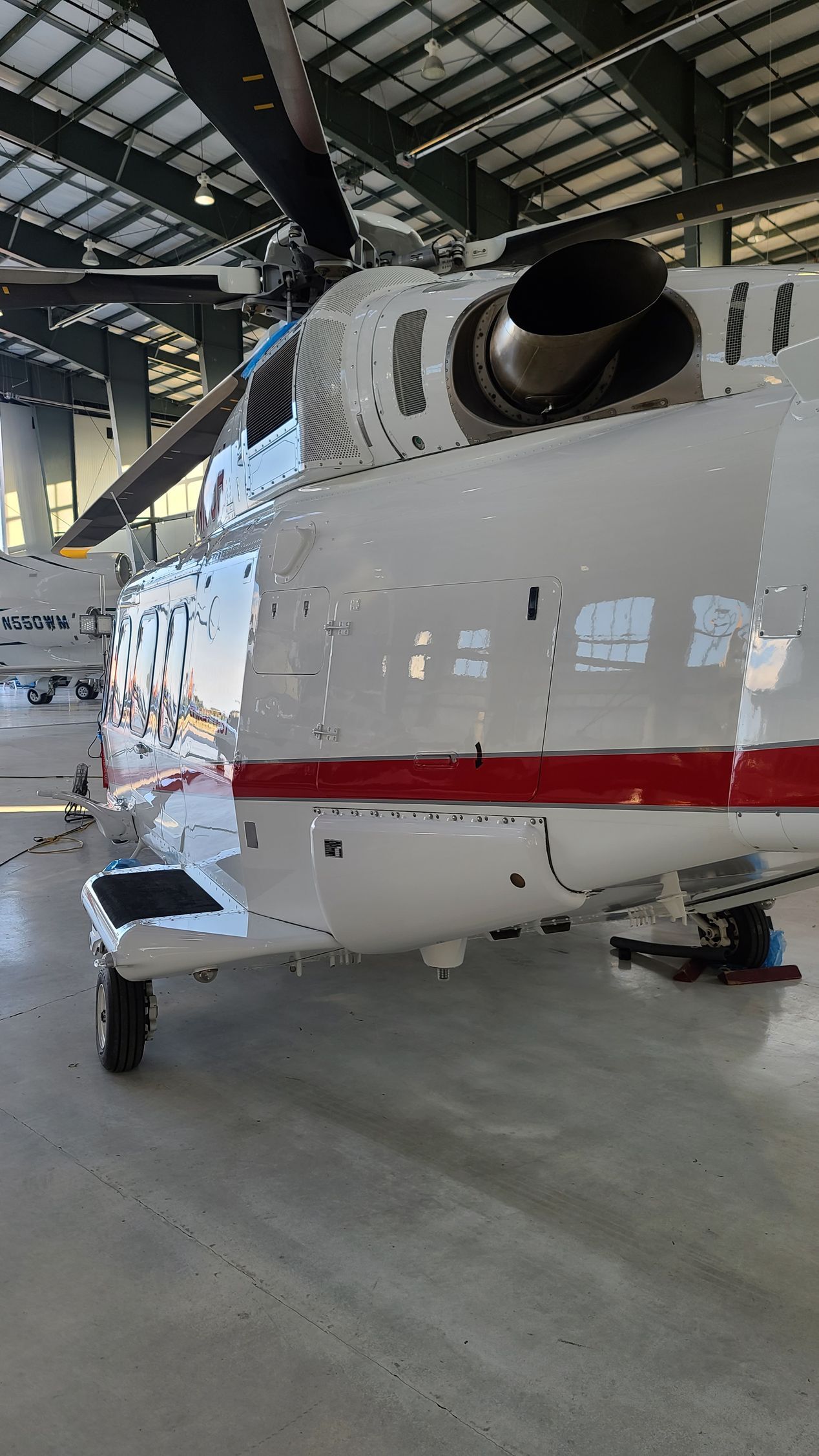 White and red helicopter in a hangar with black rotor blades and a shiny exterior.