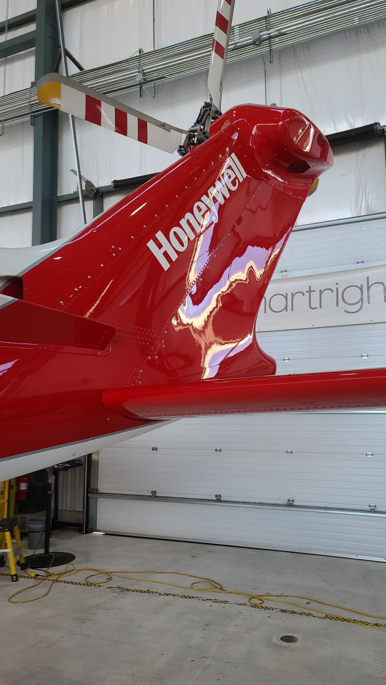 Red Honeywell helicopter tail with white stripes, reflecting light inside a hangar.