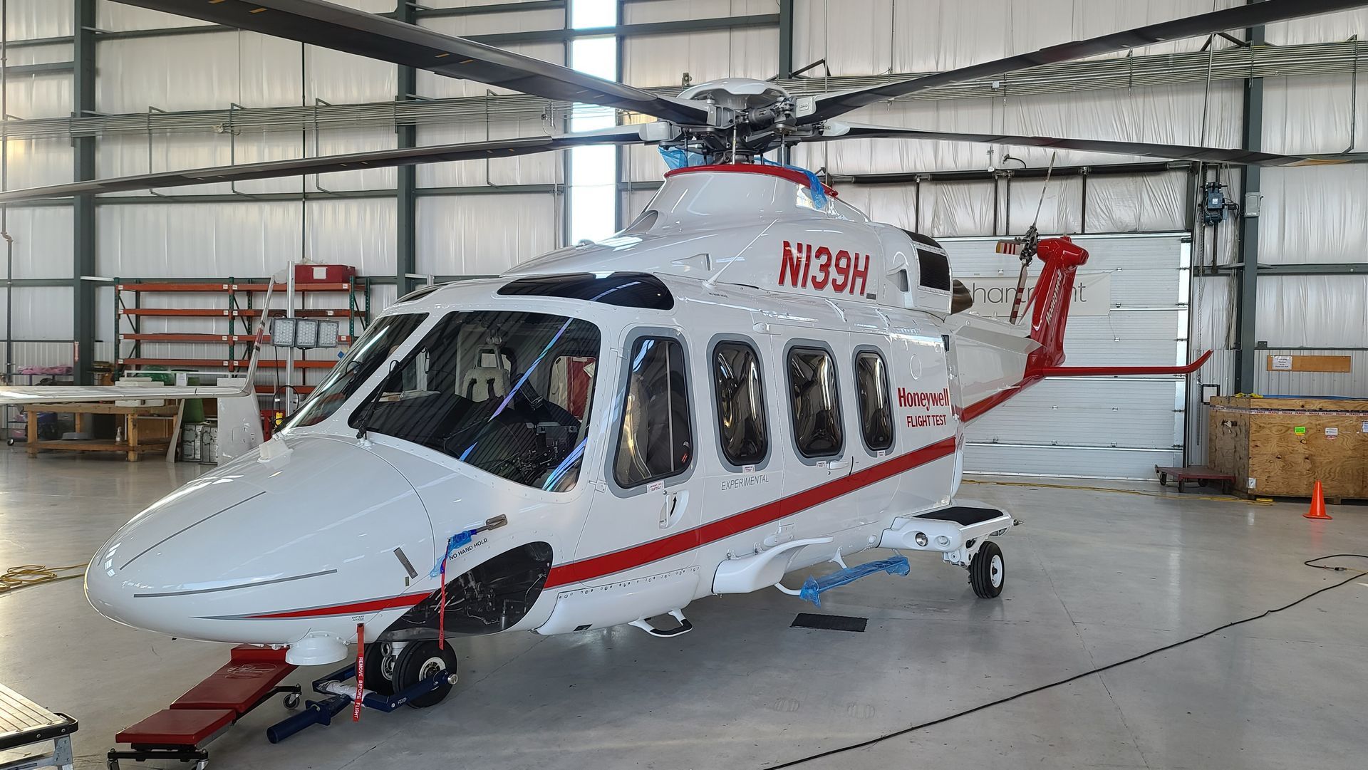 White and red helicopter inside a hangar; it has several windows and a long rotor.