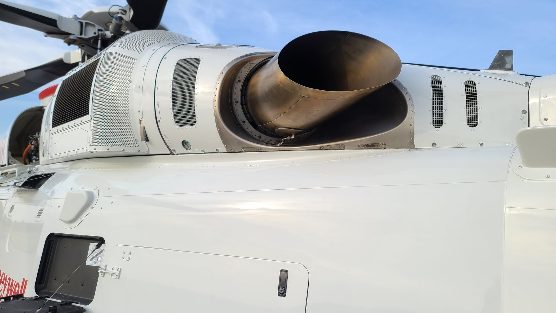 Close-up of a white helicopter exhaust with a black exhaust pipe against a blue sky.