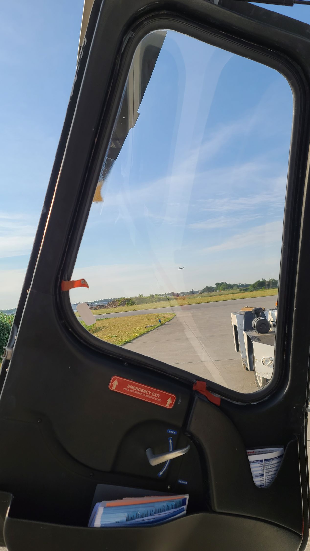 View from a vehicle's open door at an airport; blue sky, runway, and a vehicle are visible.