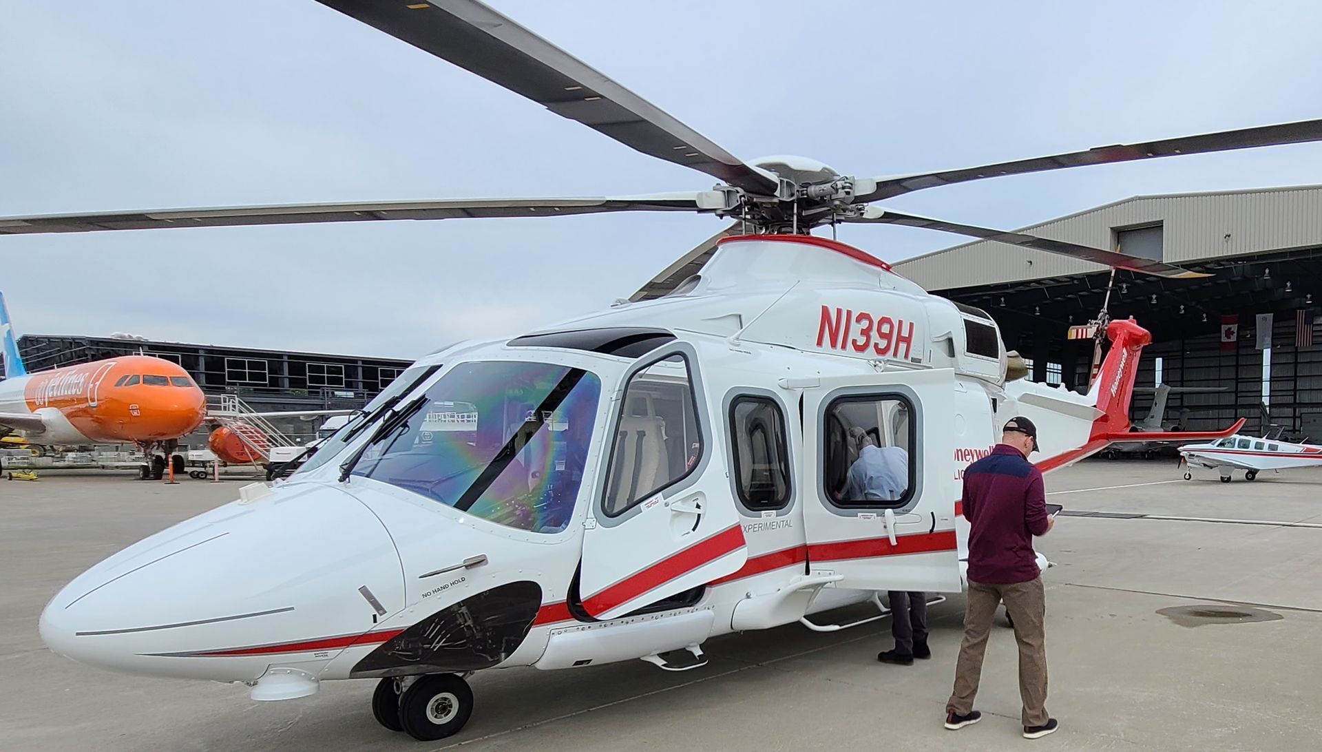 White helicopter with red accents; man standing near it on a tarmac.
