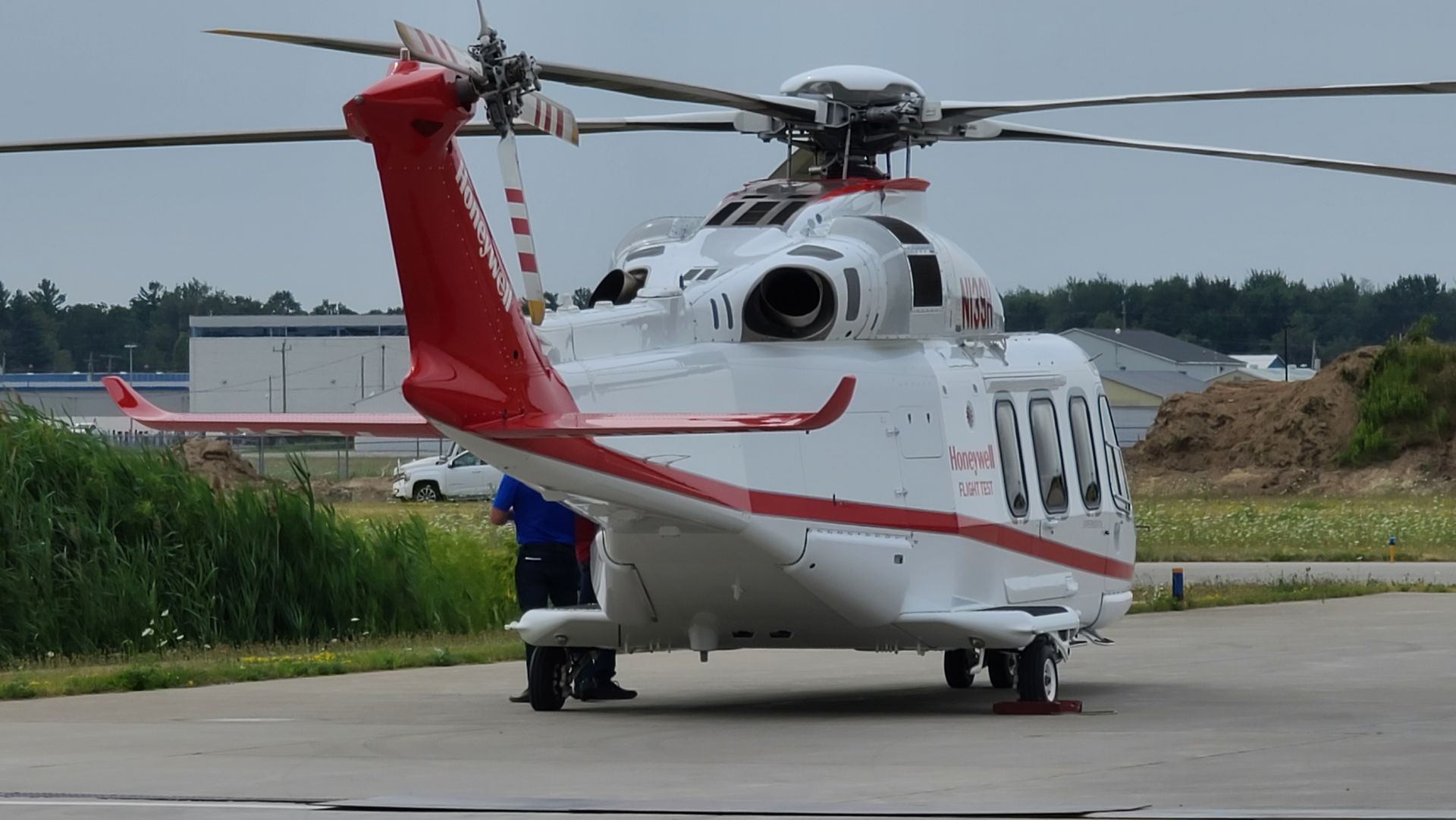 White and red helicopter on a tarmac, parked near a building and grass.