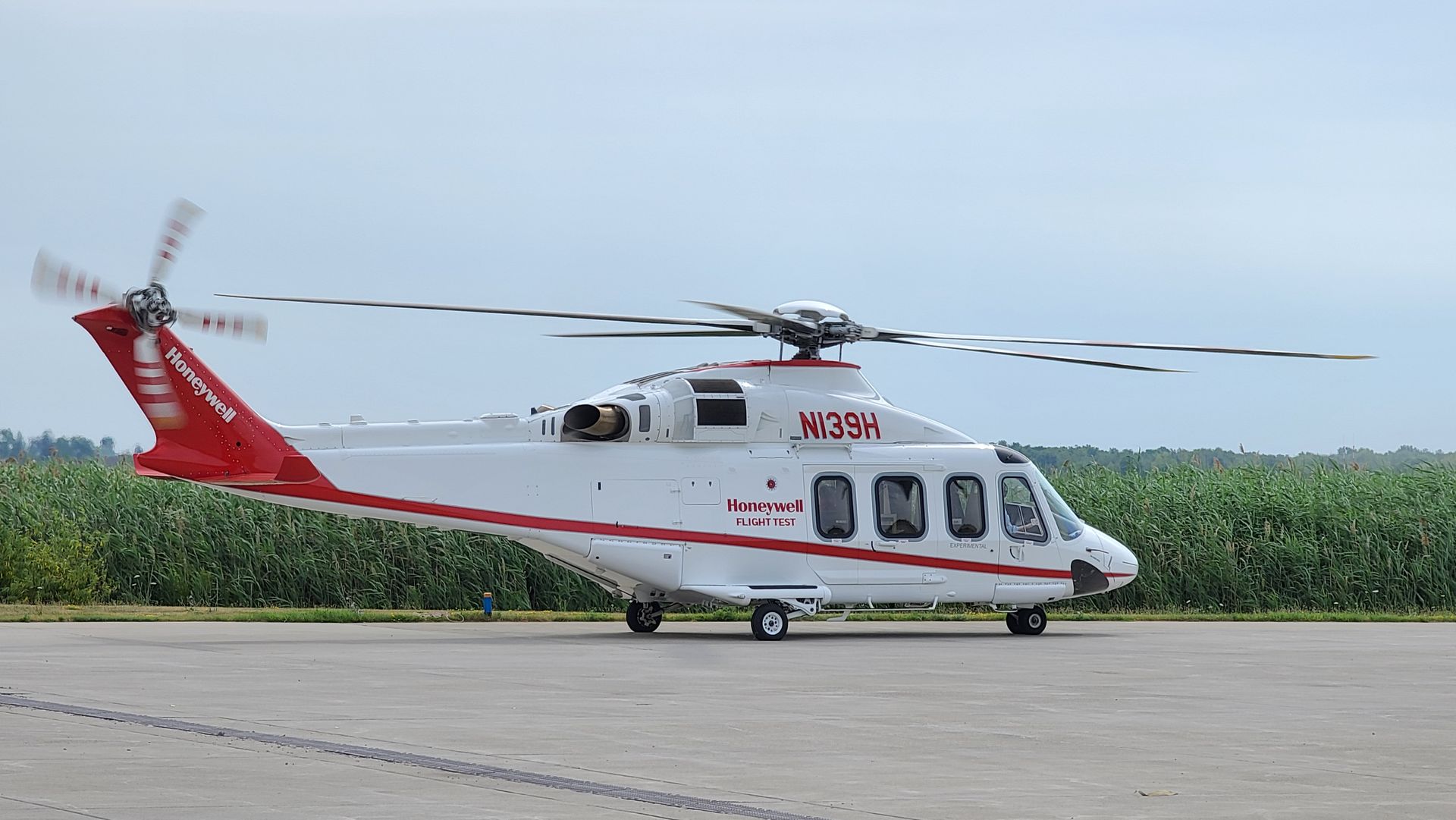 White and red helicopter on a tarmac, rotors spinning.