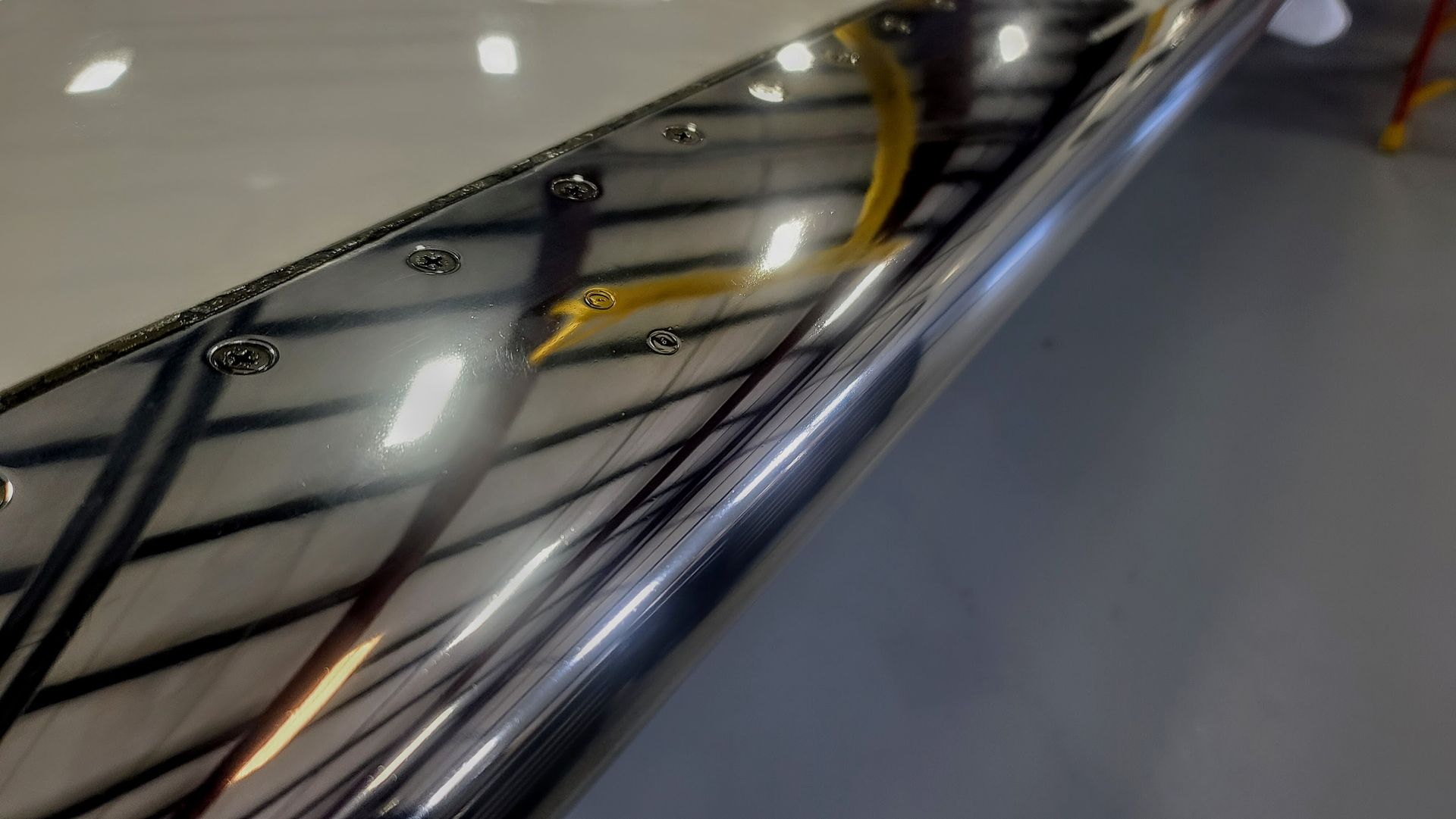 Polished metal aircraft wing reflecting a hangar interior, with rivets visible.