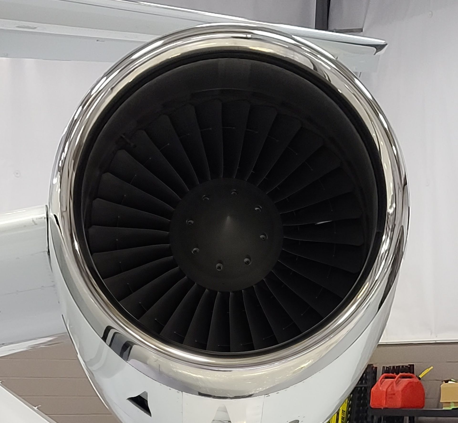 Close-up of a jet engine with a shiny silver casing. The fan blades are dark inside a circular opening.