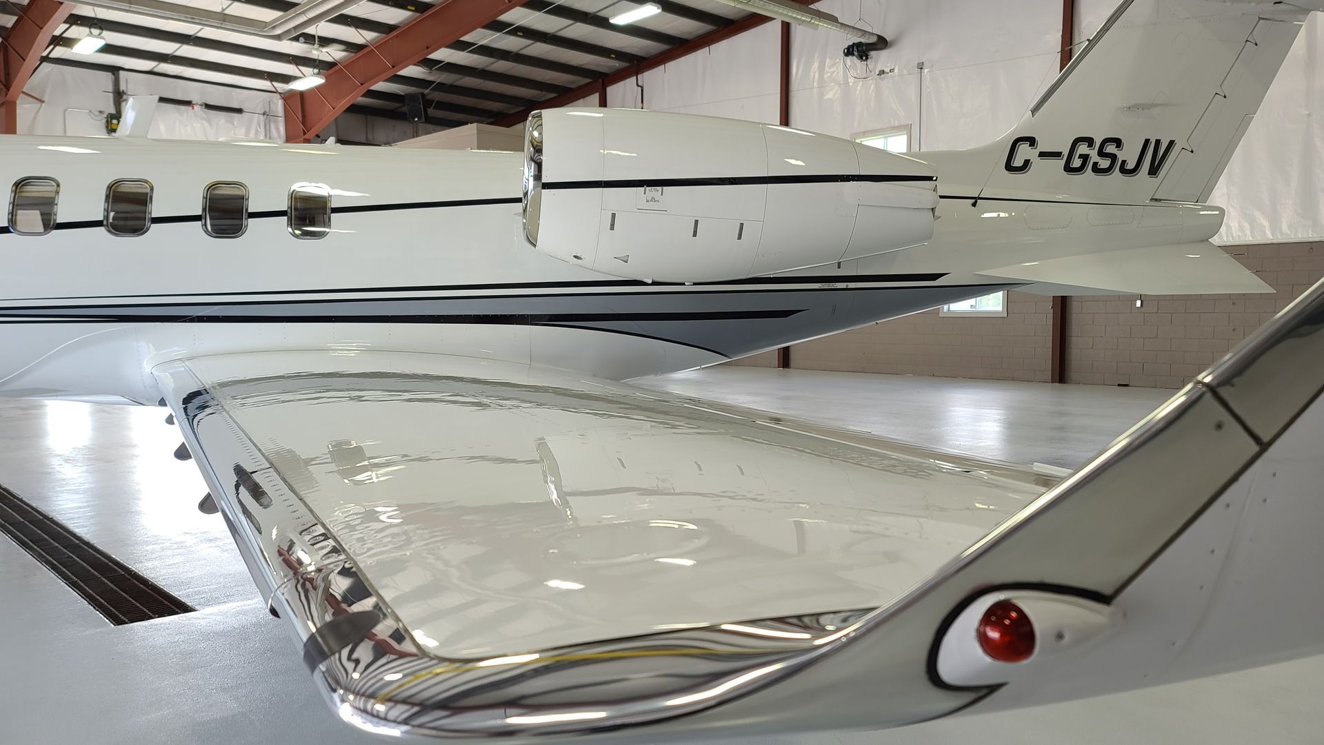 White airplane wing with reflective metal trim and red light, inside a hangar.