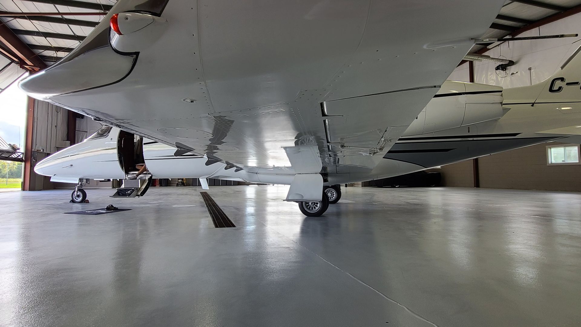 A white private jet sits inside a hangar. The undercarriage and wing are visible.
