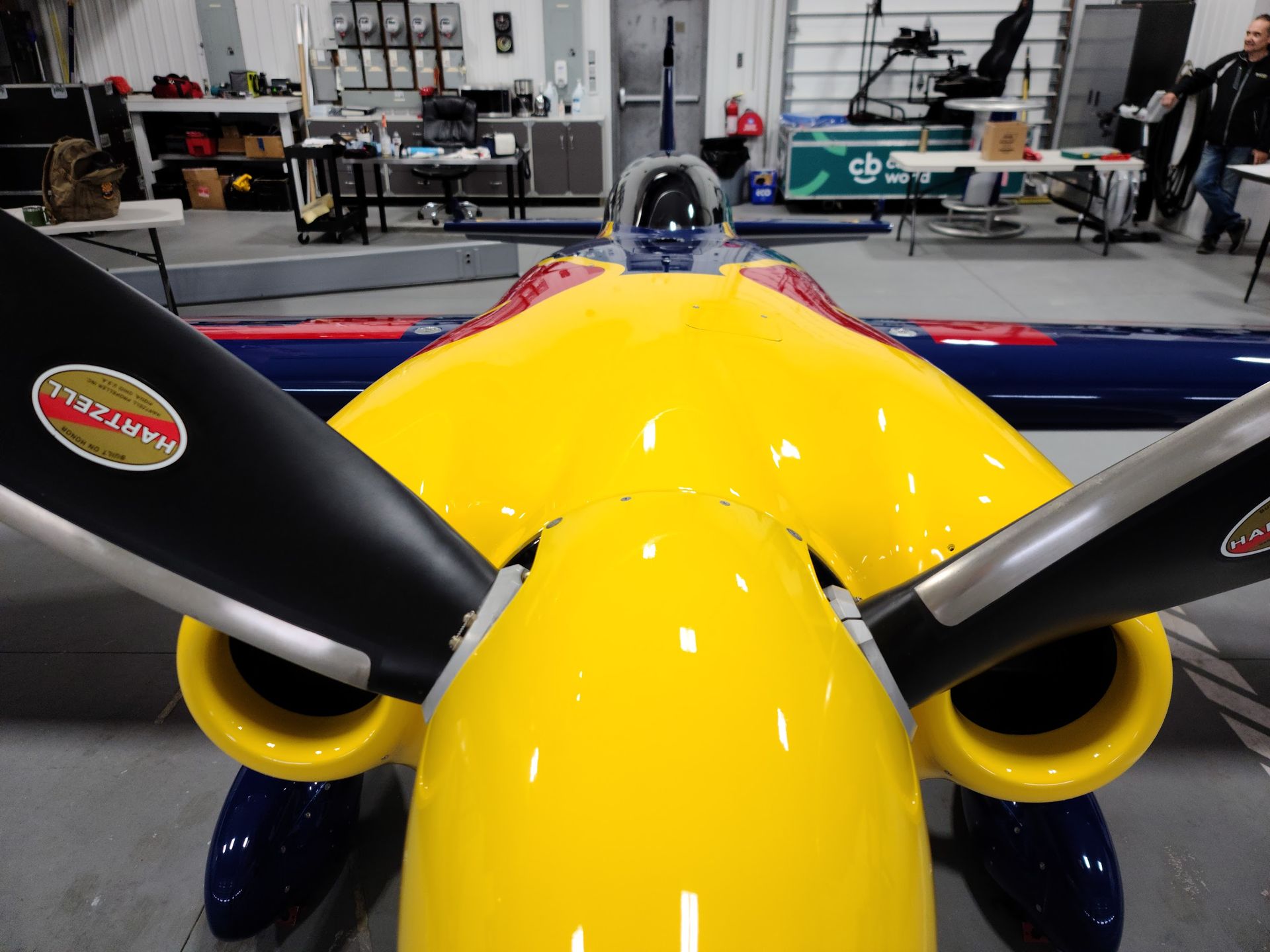 Yellow and blue aerobatic plane, close-up of propeller and fuselage in a hangar.