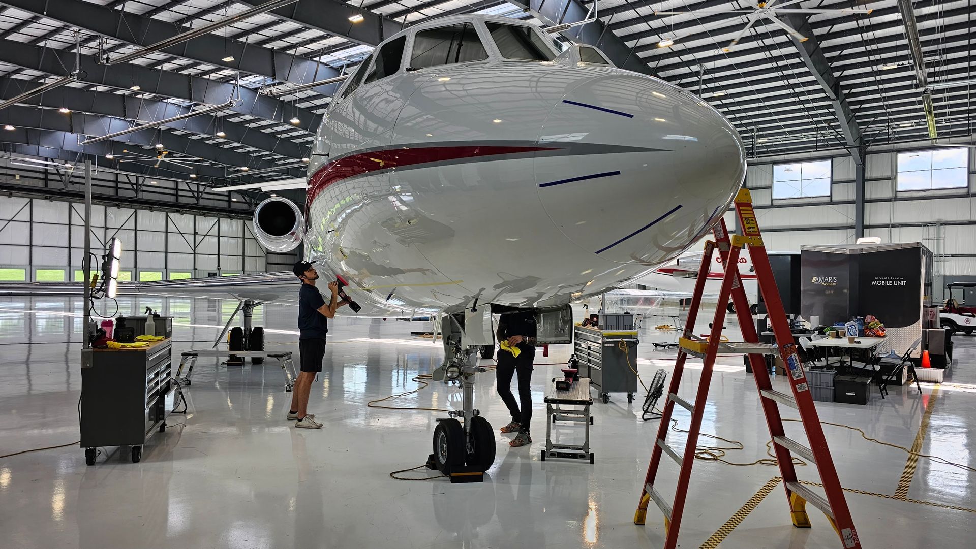 Airplane in a hangar, being worked on by several people with tools, a ladder, and machinery.