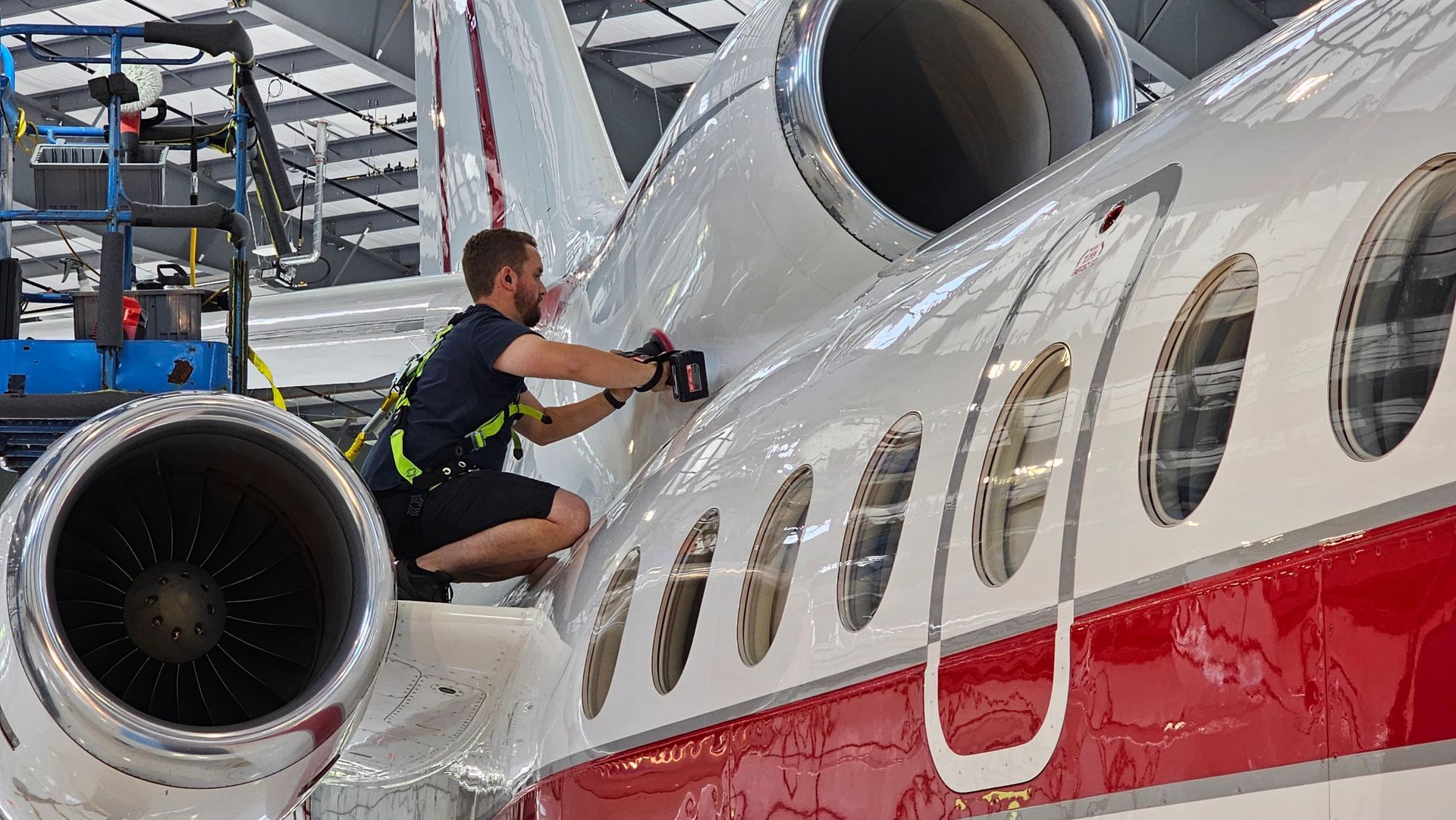 A mechanic working on the side of a white and red private jet inside a hangar.