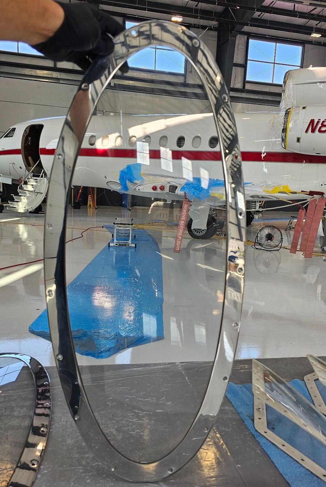 Person holding a shiny, oval metal frame in a hangar with a partially visible airplane.