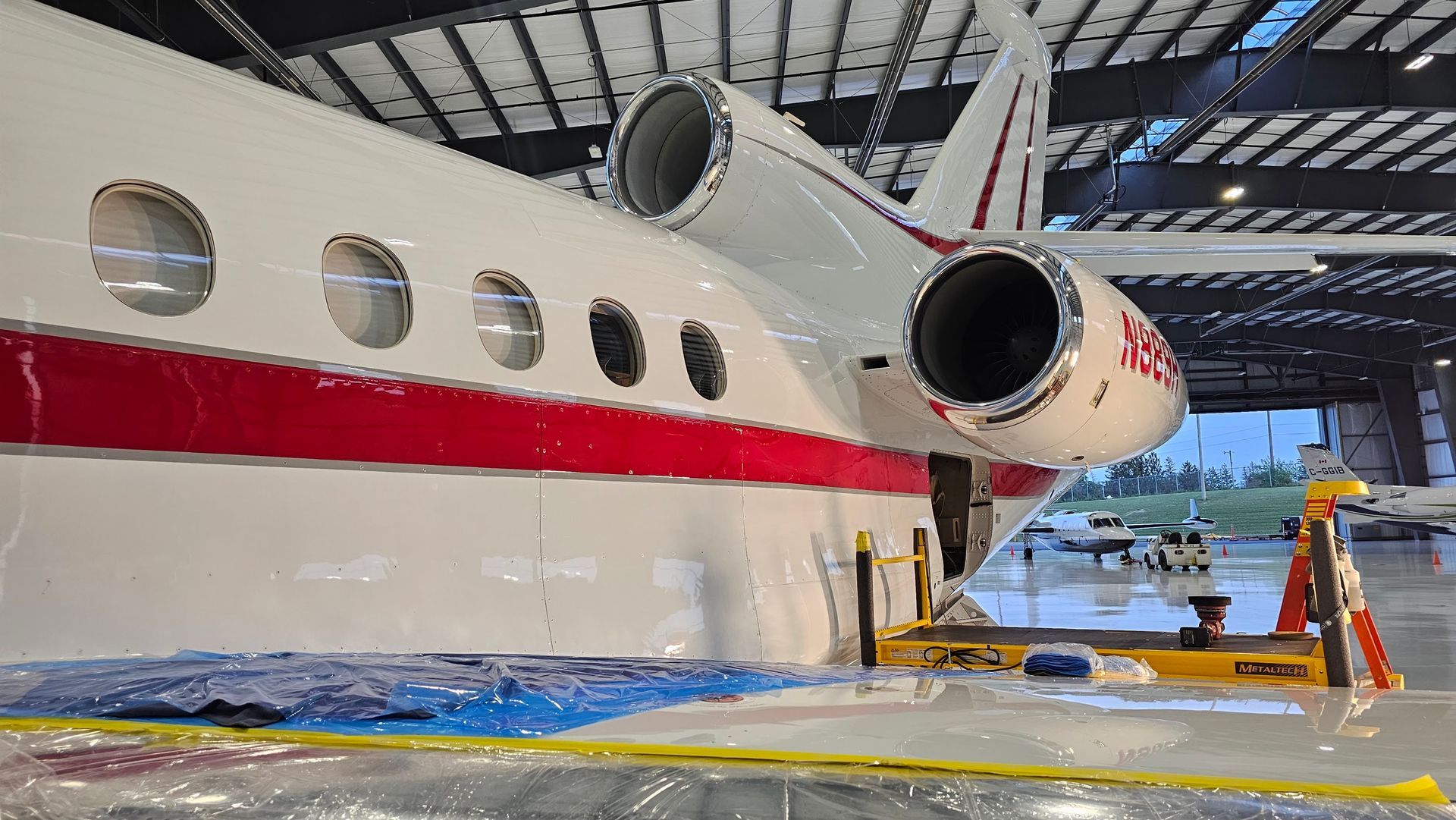 White and red private jet parked inside a hangar, with open door and support platform.