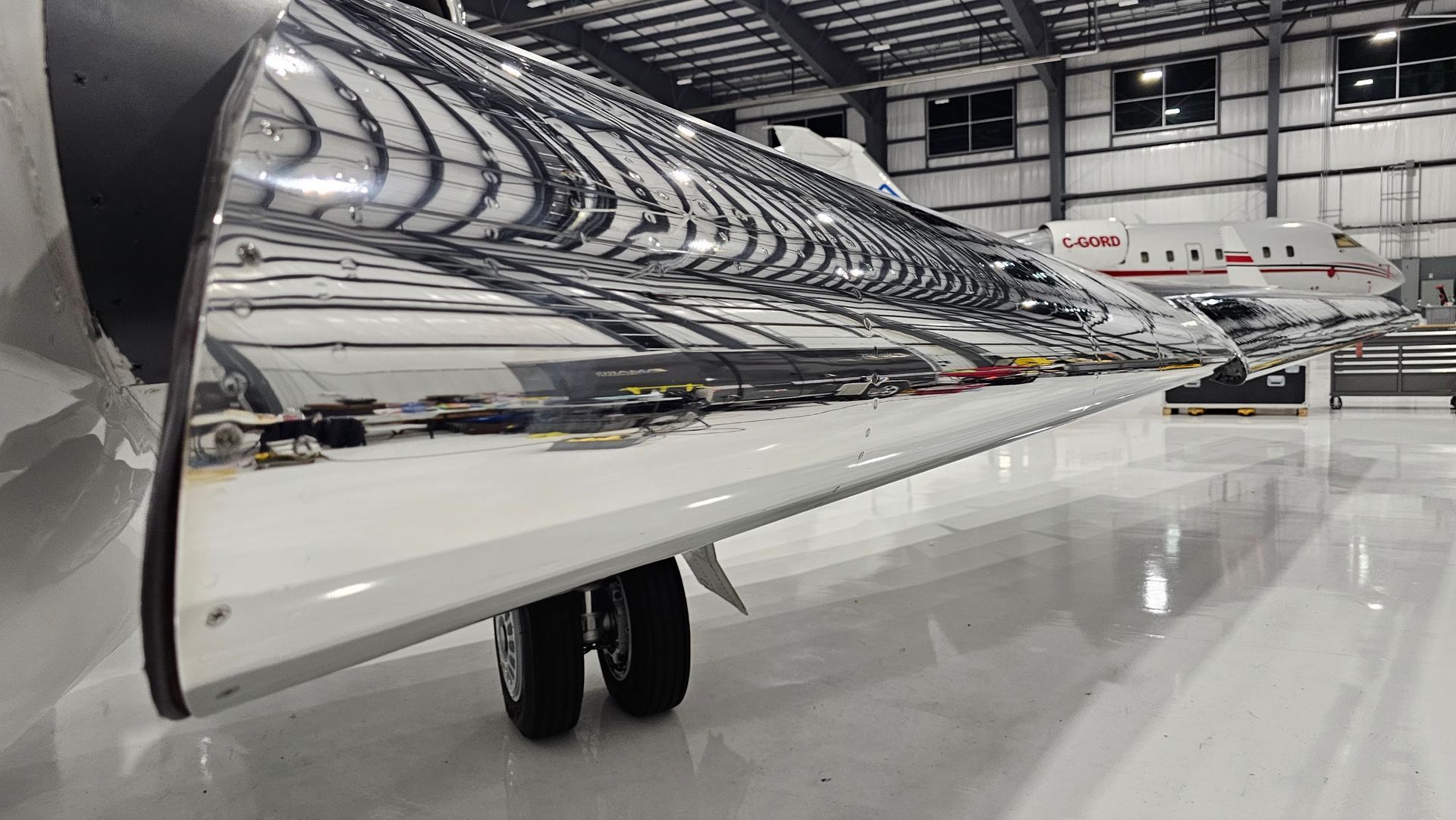 Airplane wing reflecting a hangar, with landing gear visible.