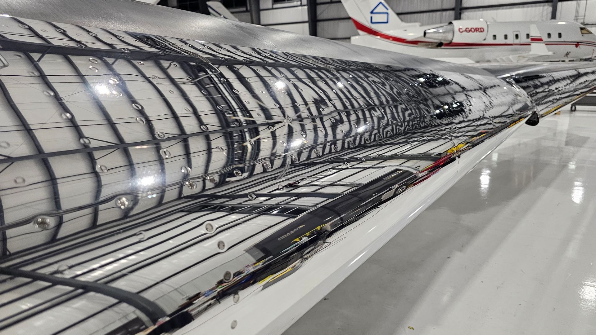 Aircraft wing, shiny metal surface, hangar interior, reflection of overhead structure.