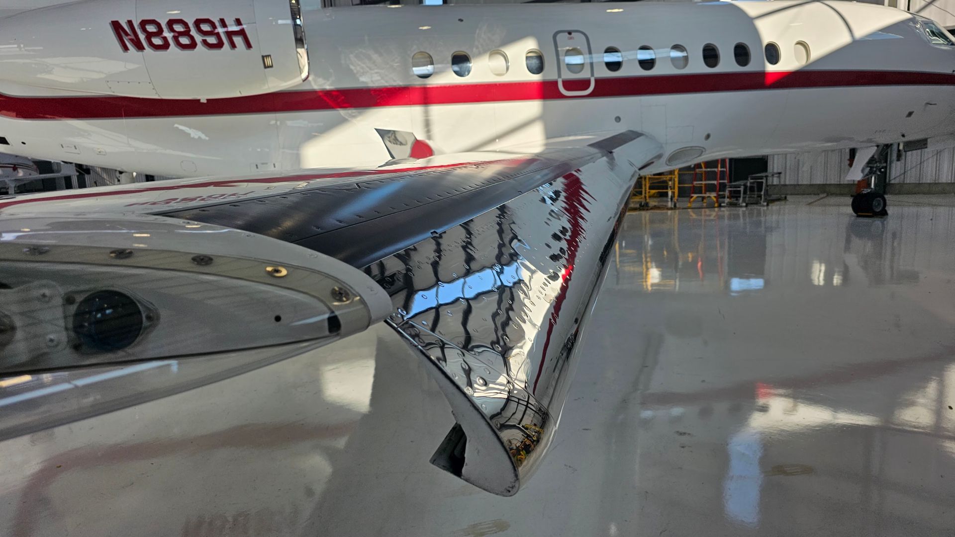 Aircraft wing with a reflective, metallic surface; red and white fuselage visible in the background inside a hangar.