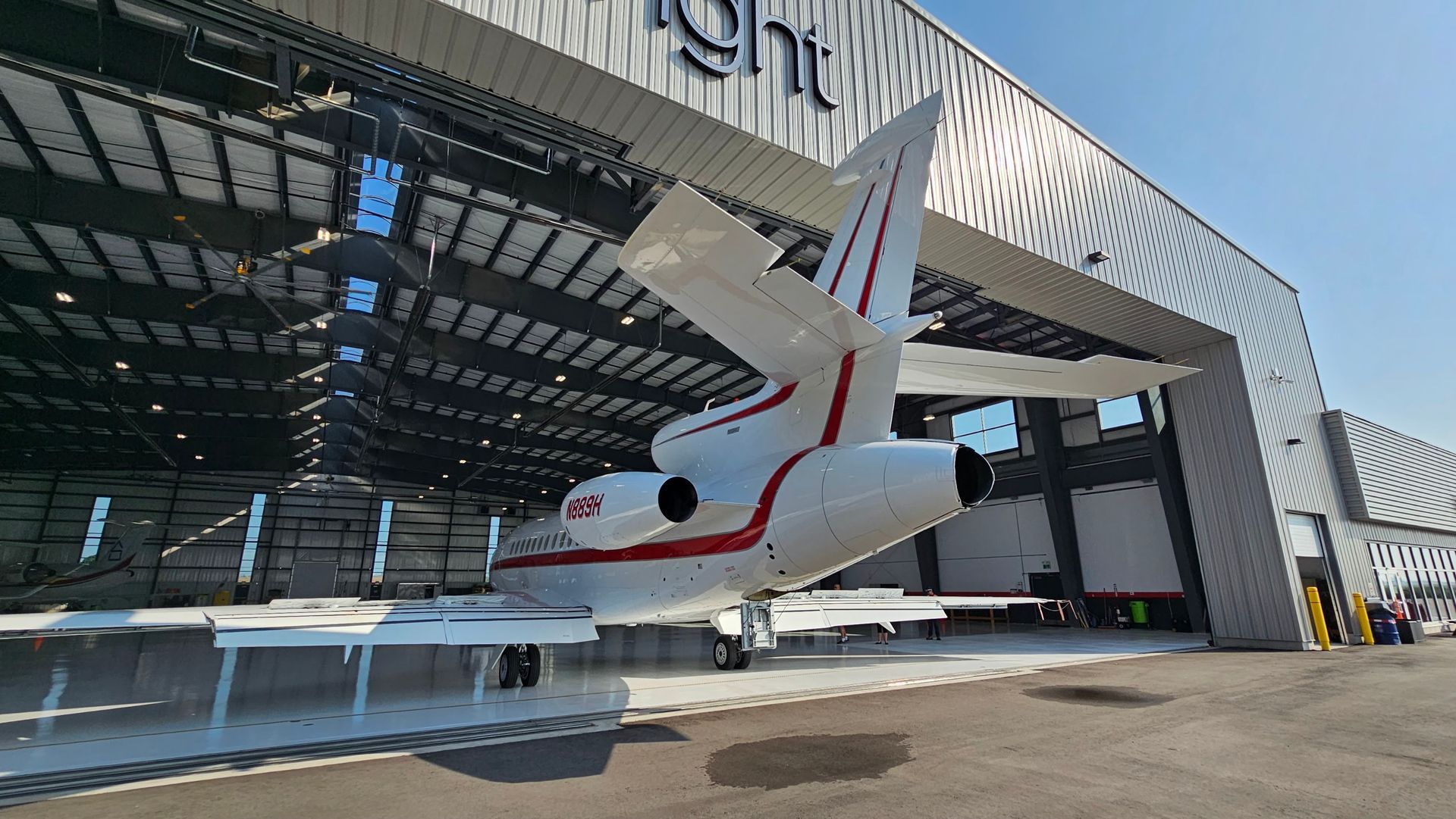 White and red private jet in a hangar. The tail is angled, and the wings are visible.