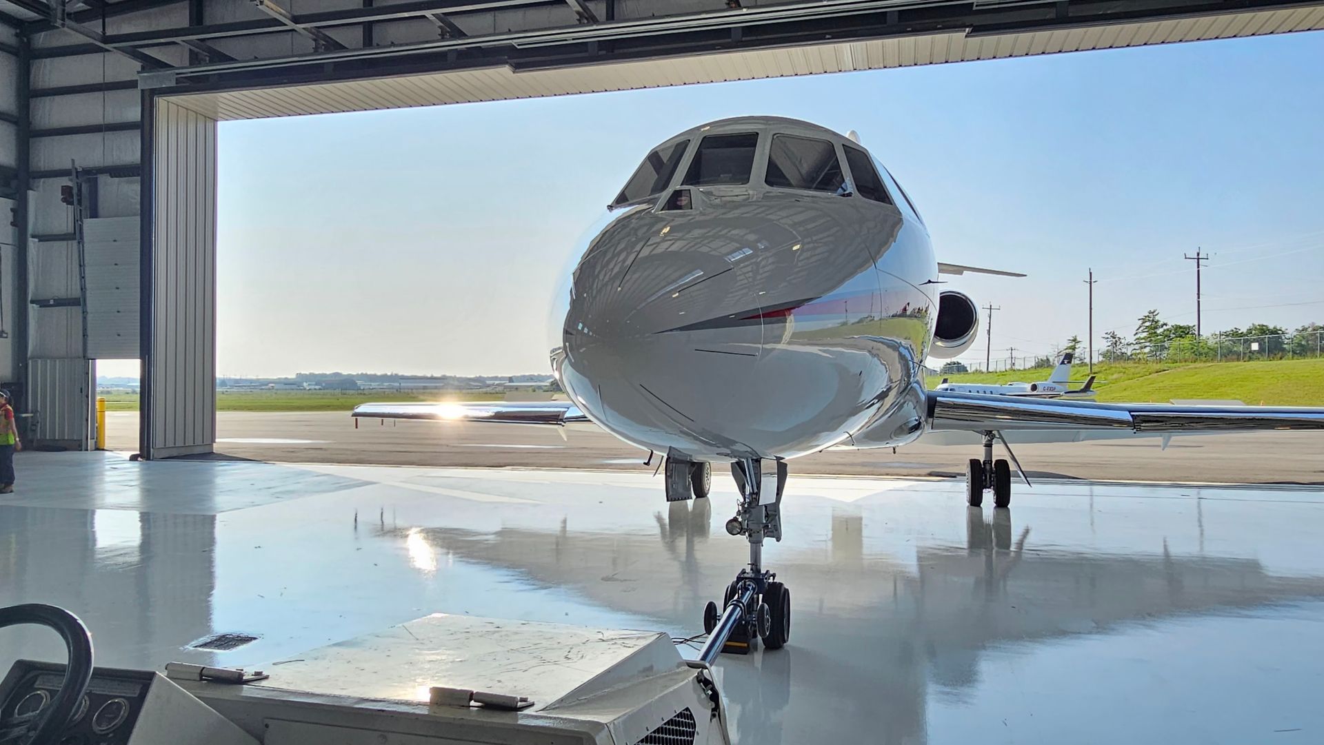 Jet airplane parked in a hangar with the door open, reflecting the sun.