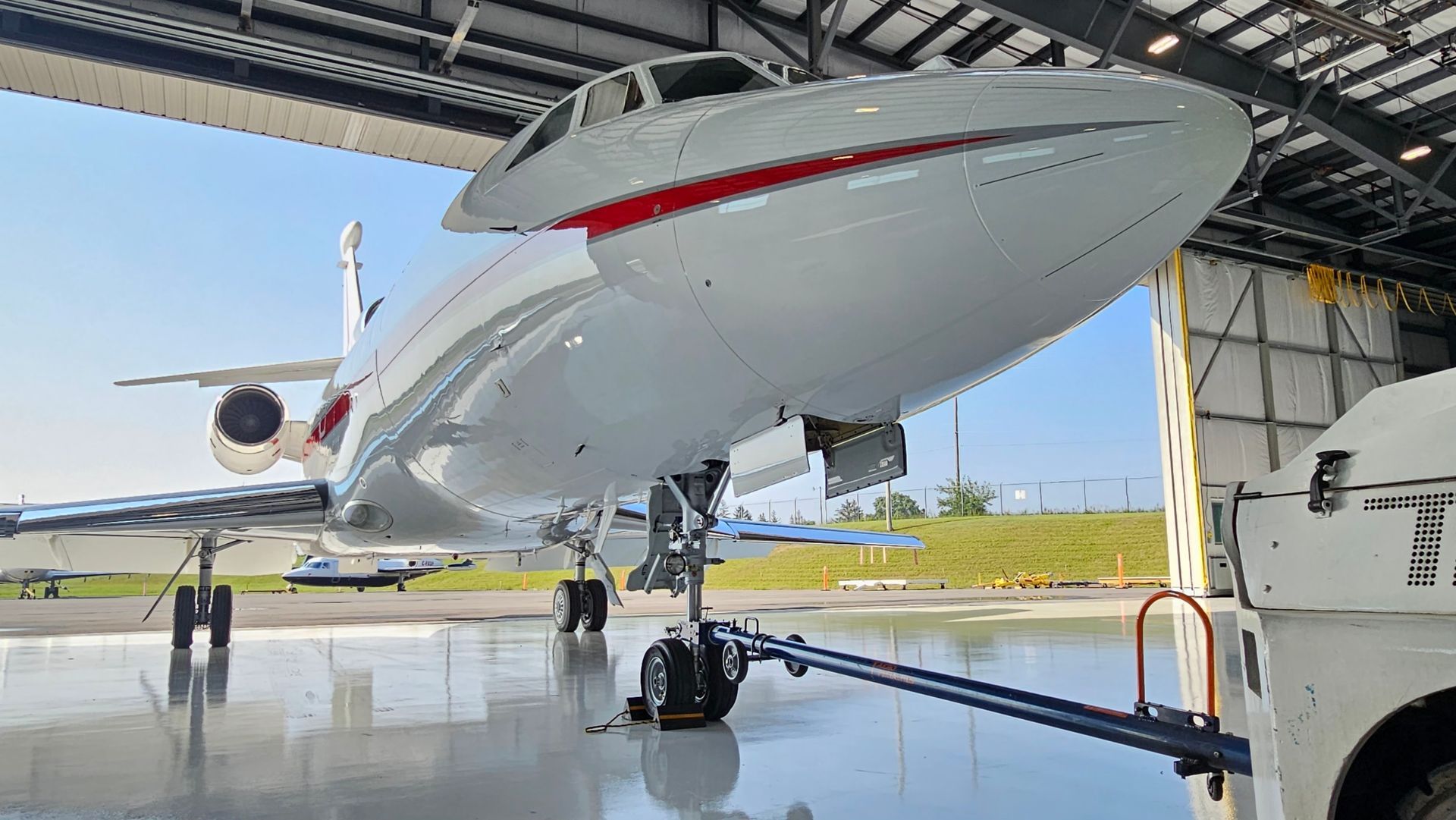 White and red private jet parked inside a hangar, with tow bar connected.