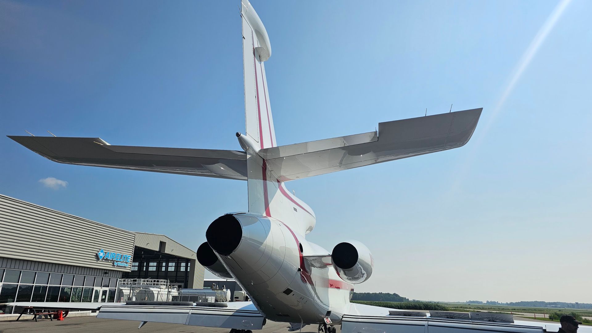 Rear view of a white private jet on the tarmac with a blue sky background.