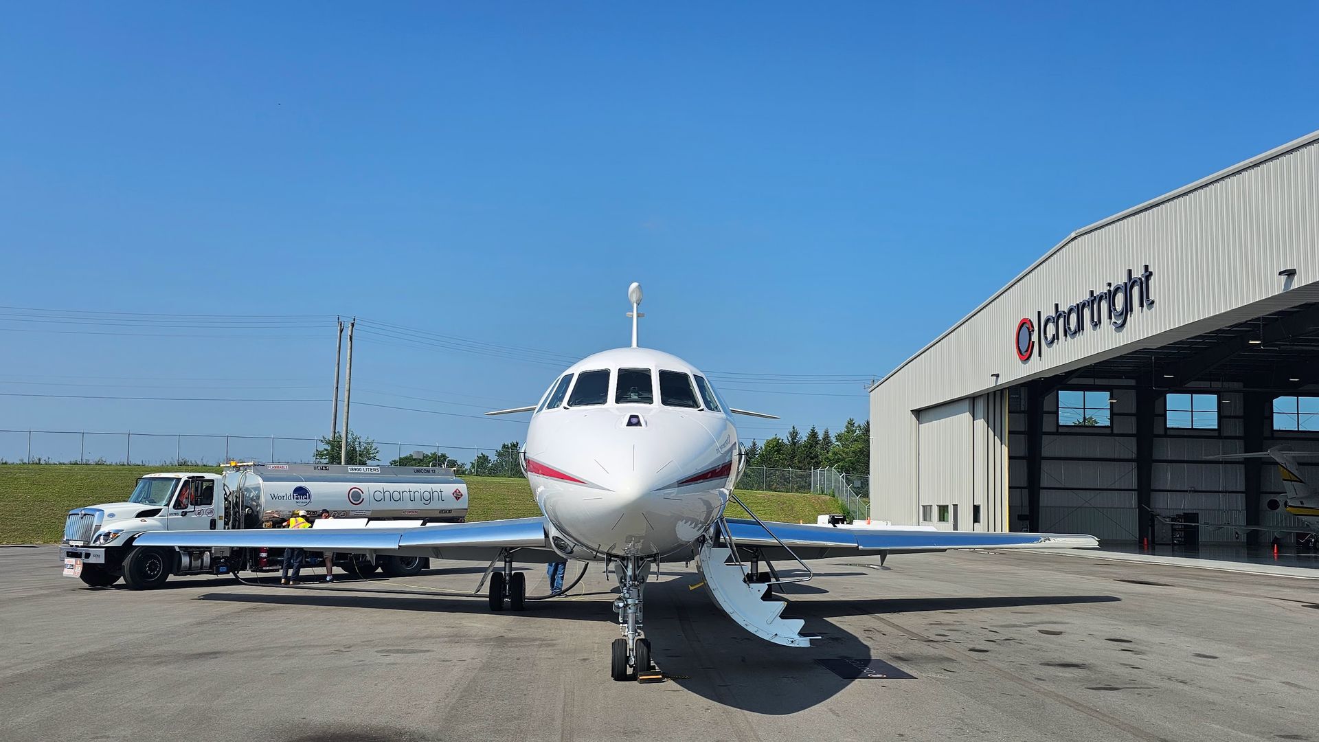 A private jet is parked outside a hangar next to a fuel truck on a sunny day.