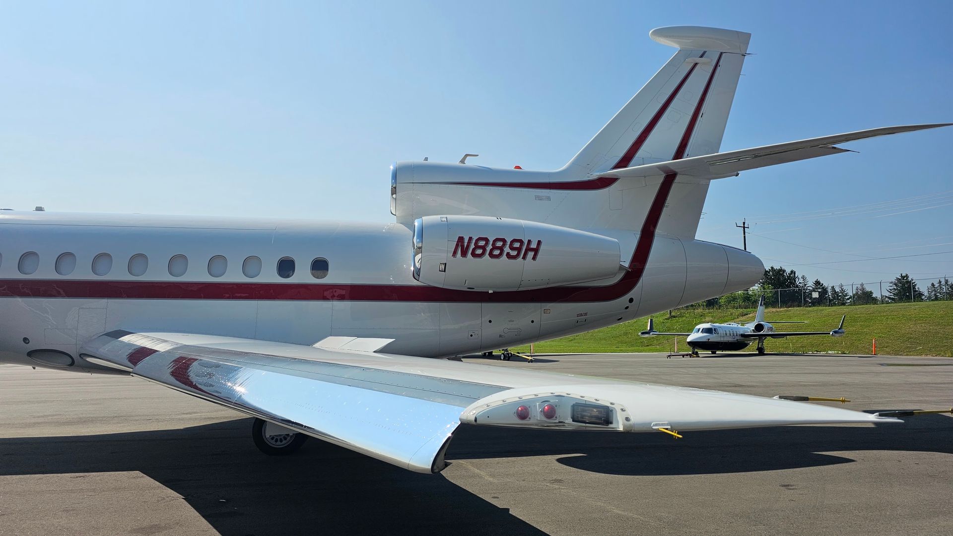 White and red private jet on a tarmac, with a small jet in the background under a blue sky.