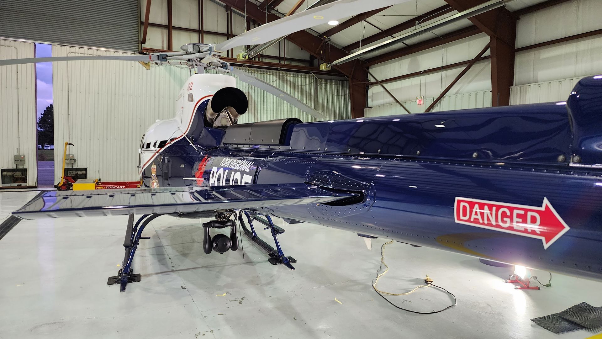 A person working on a dark blue helicopter inside a hangar.