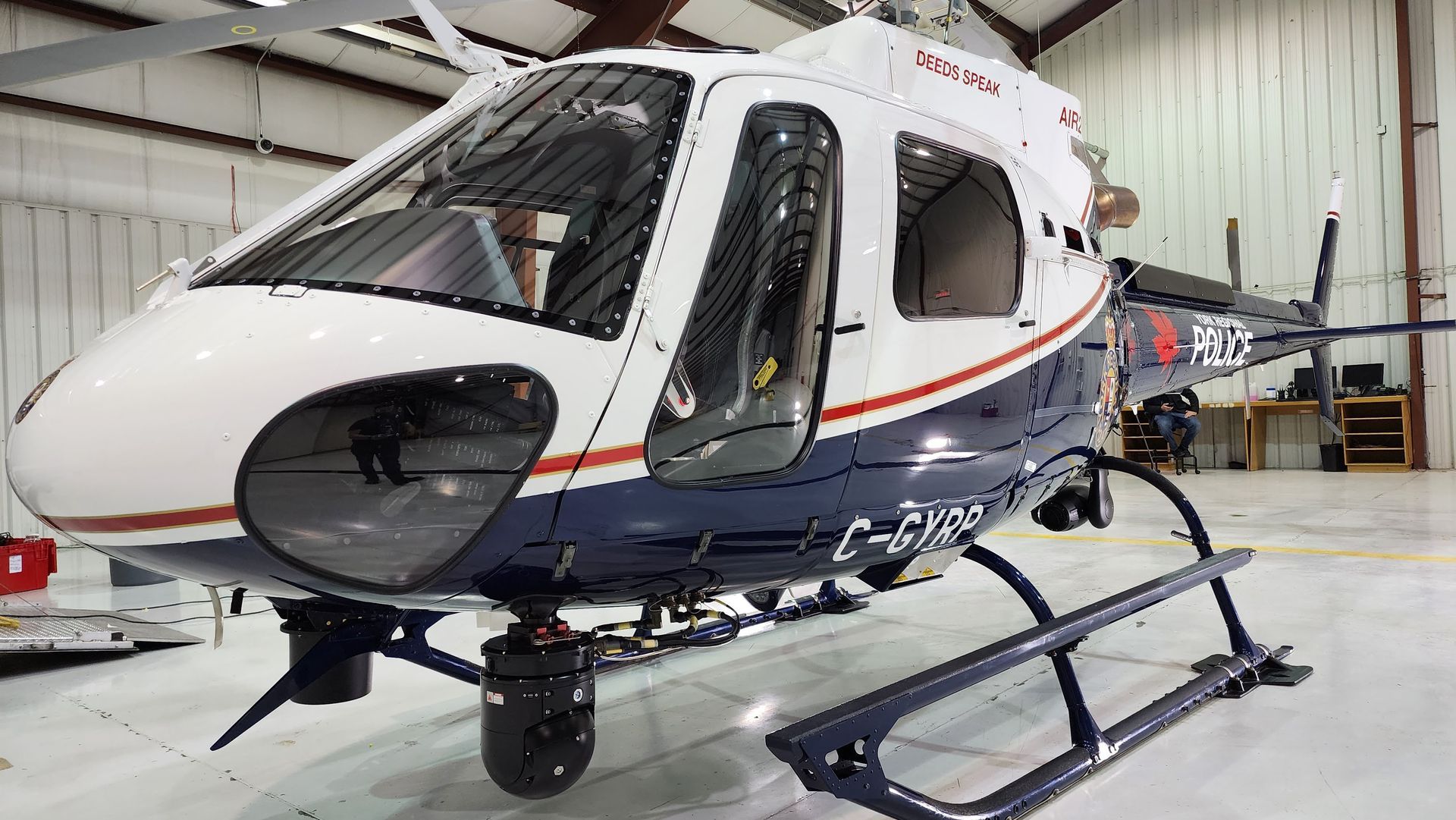 White and blue helicopter in a hangar with the door open.